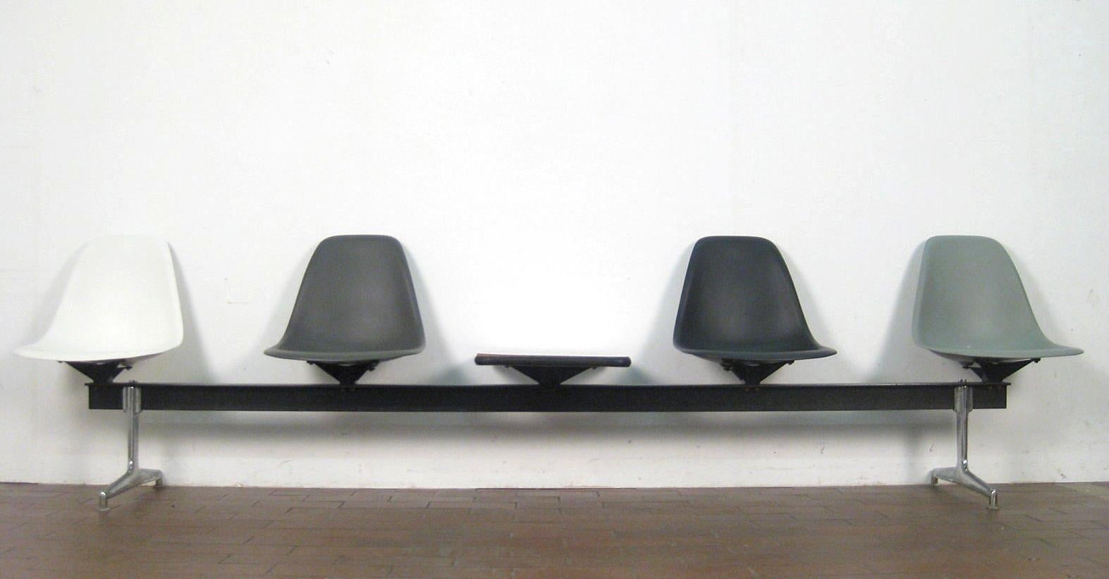 Rare tandem shell seating designed by Charles & Ray Eames and produced by Vitra of Switzerland. This piece features four different colored plastic seats and a table mounted on shock mounts to a black painted steel T-bar raised on aluminum legs.
