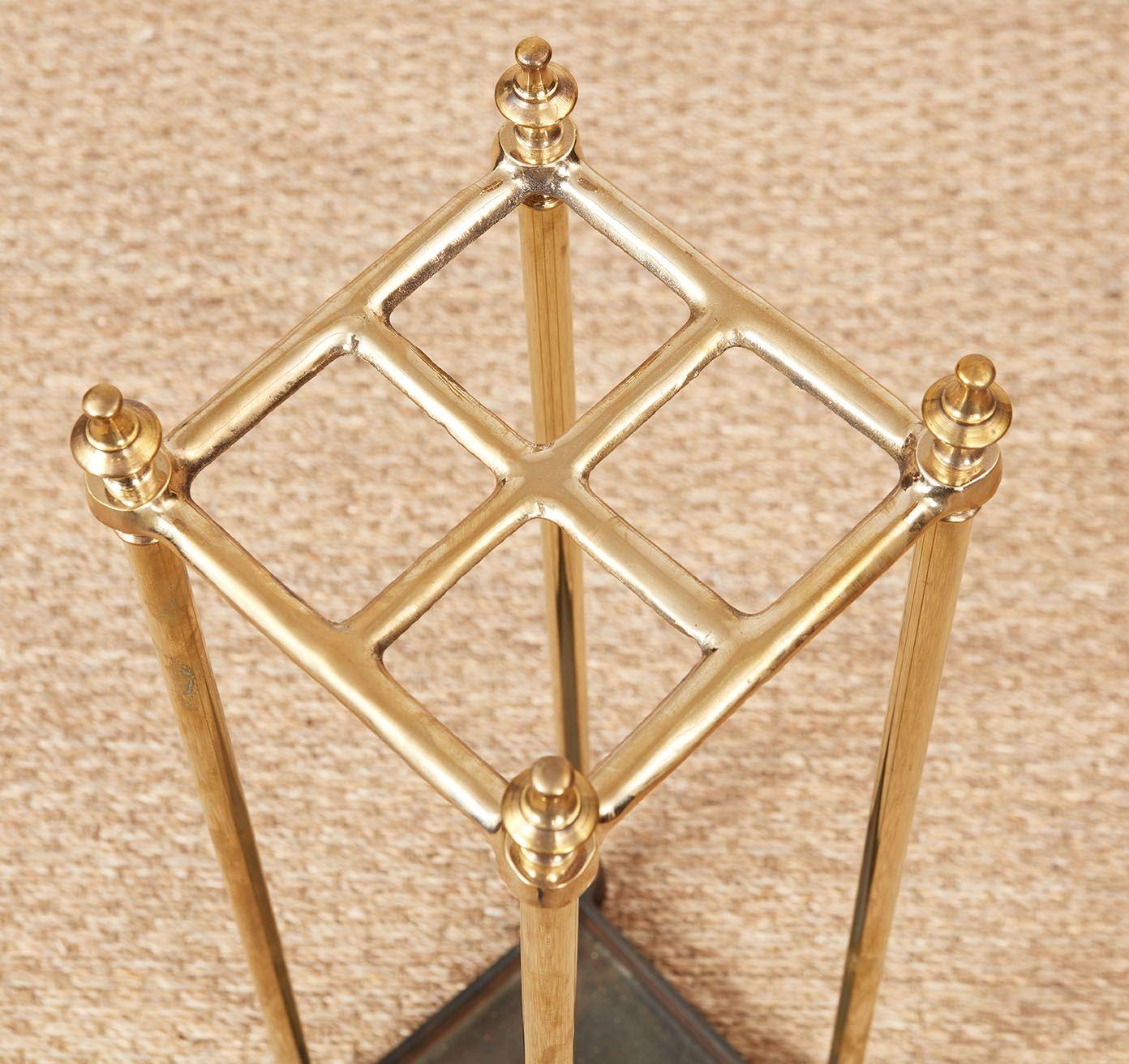 Un portaombrelli con piano quadrato a quattro sezioni in ottone su gambe in ottone inserite in un vassoio di sgocciolamento in ferro nero con raccordi angolari rotondi, con terminali e estremità delle gambe in ottone.  Circa 1900.
