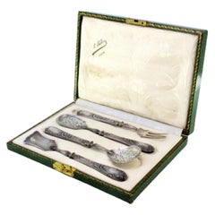 Four silver dessert pieces with cut-out shells and raised floral handles, cased