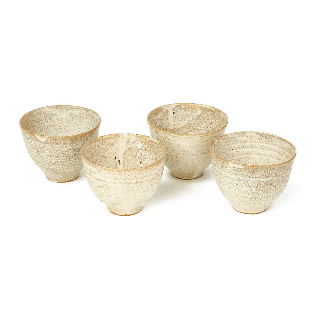 A stylish set four finely potted Studio Pottery bowls of simple identical rounded shape on narrow rounded feet and decorated in oatmeal glazes with areas of white and small black inclusions. The bowls do not appear to be marked. Maker unknown,