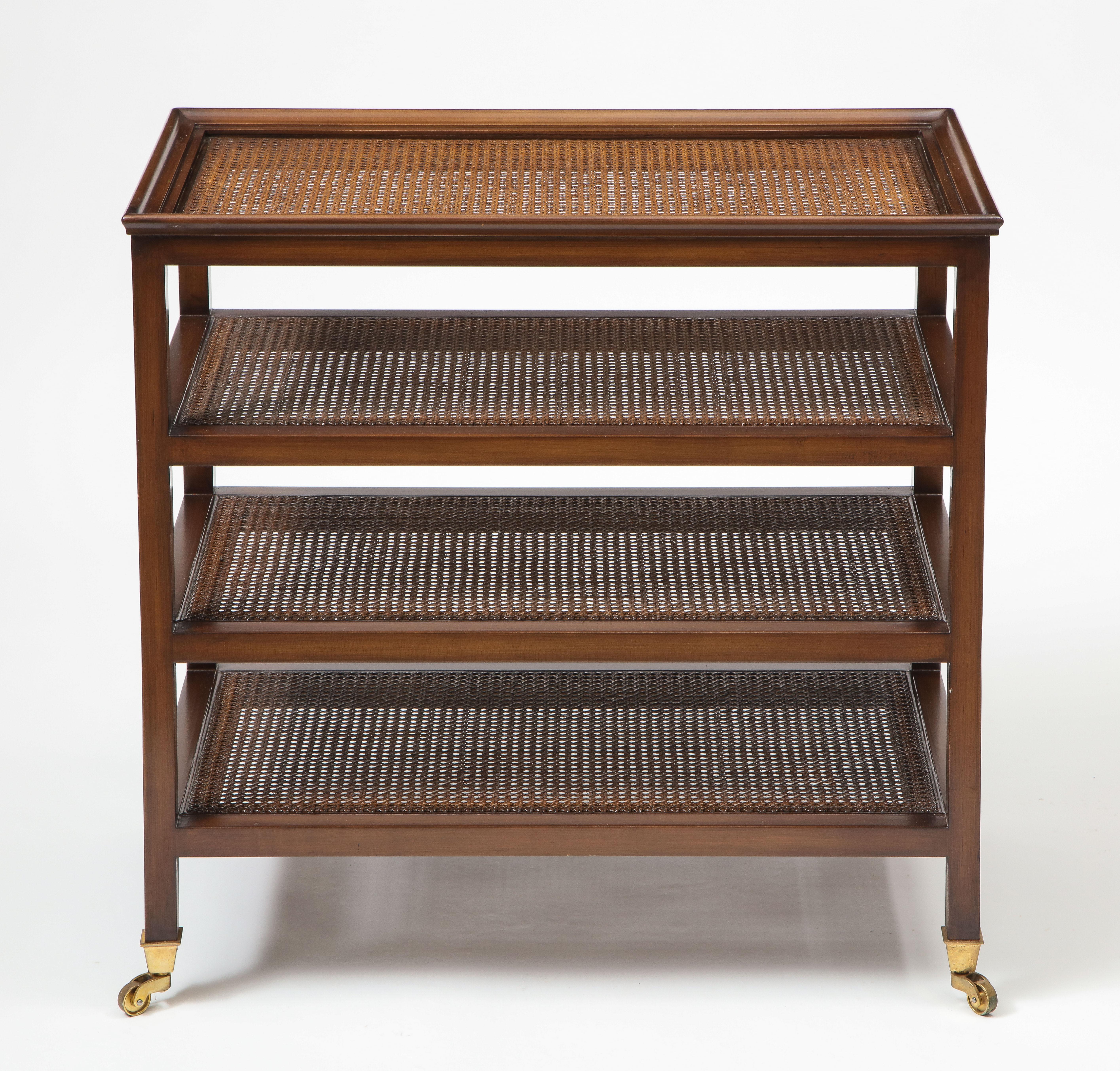 The wood étagère stained in walnut with four caned shelves; on brass caps and casters.