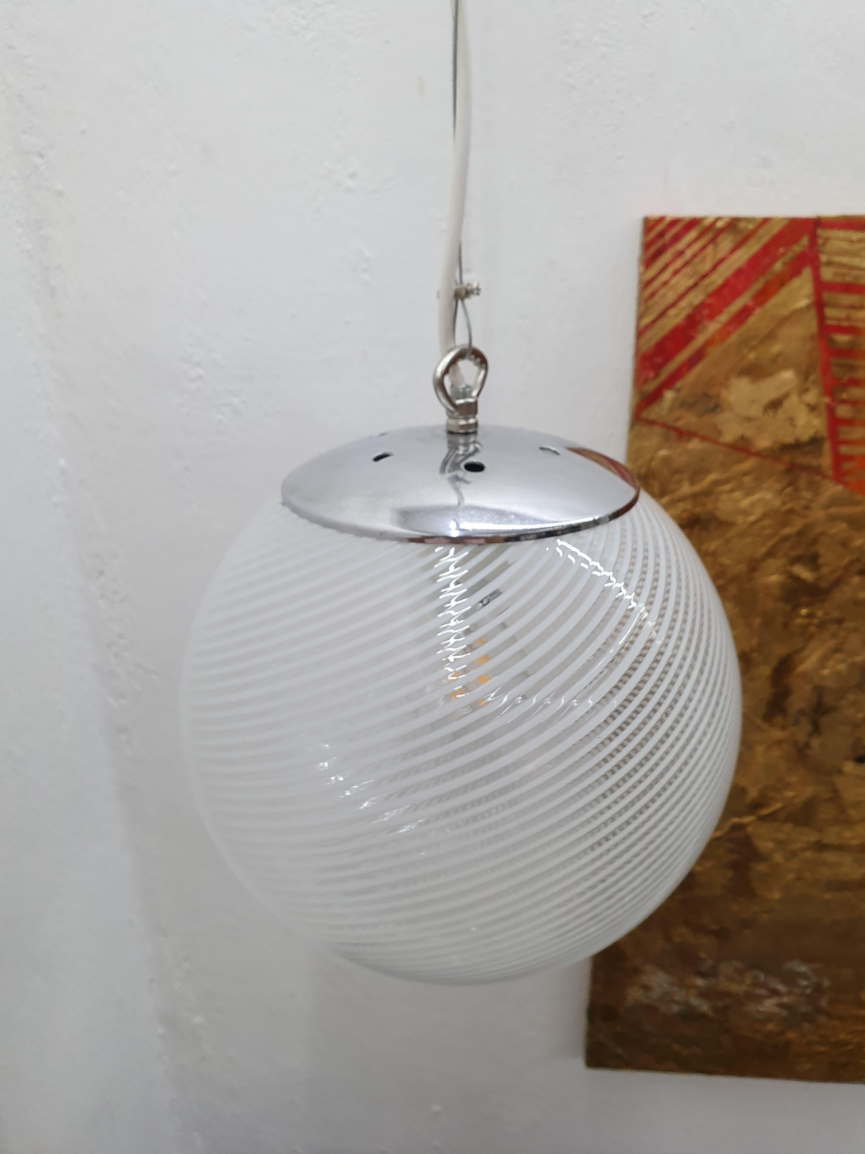 Beautiful pendant sphere, in clear and white striped hand blown Murano glass, style of Venini, circa 1970's.

Please look at the photos to really appreciate the beautiful shadow this kind of lamps cast.
There are 4 identical lamps available
Height
