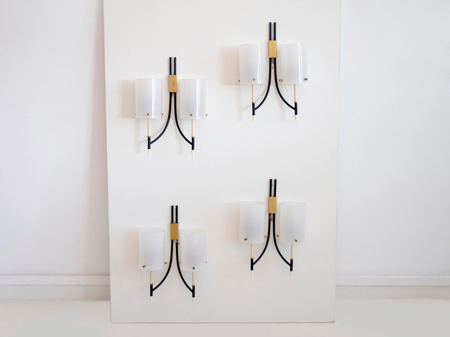 Wall lamps of black painted metal, brass details and white cylindrical Perspex shades, attributed to Casey Fantin. Each lamp with two light sockets. Four lamps available, price per one.
  