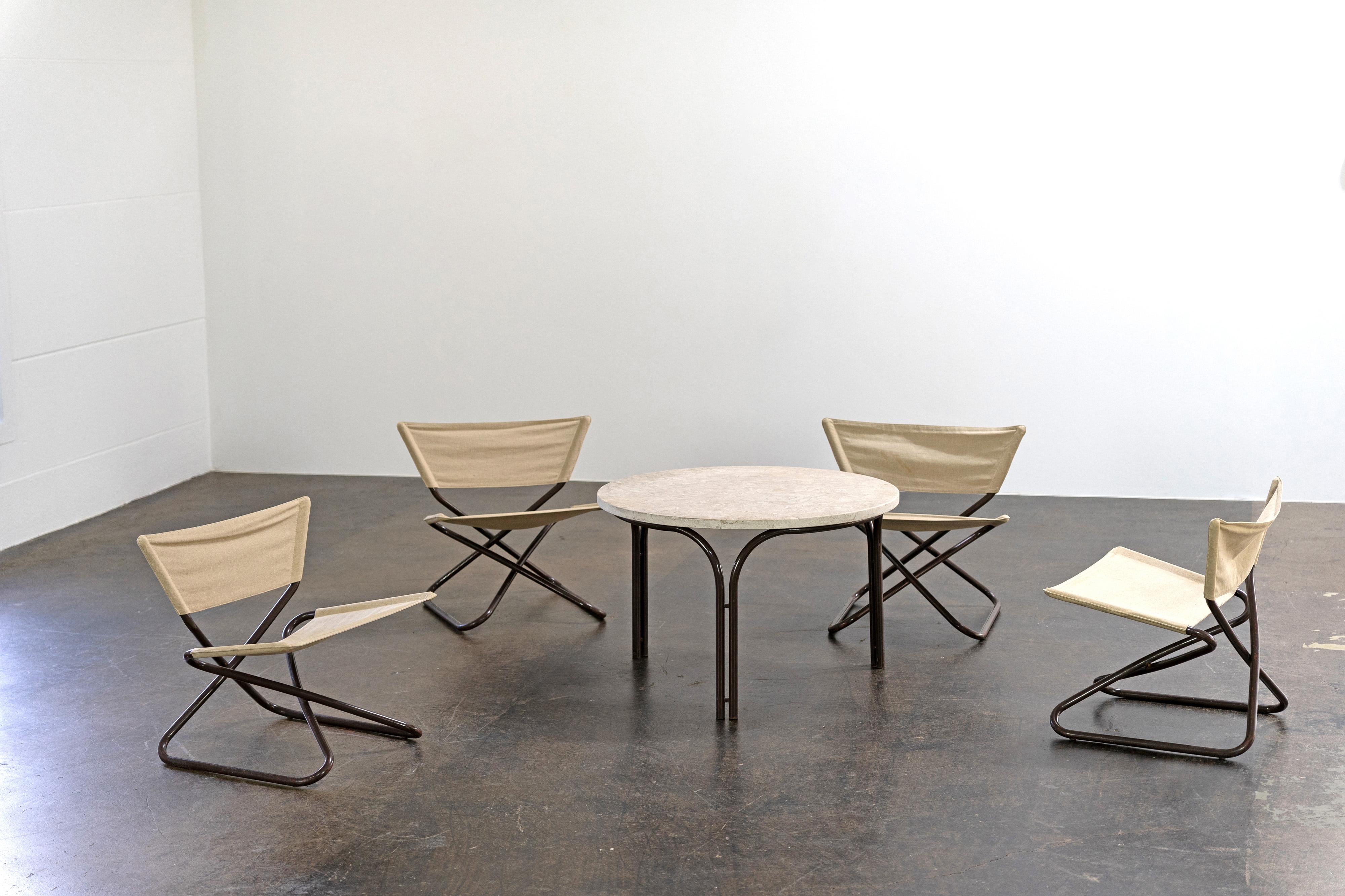 Rare set of four folding lounge chairs by Erik Magnussen, made of brown lacquered tubular steel with linen covers, and a table with a travertine table top. 