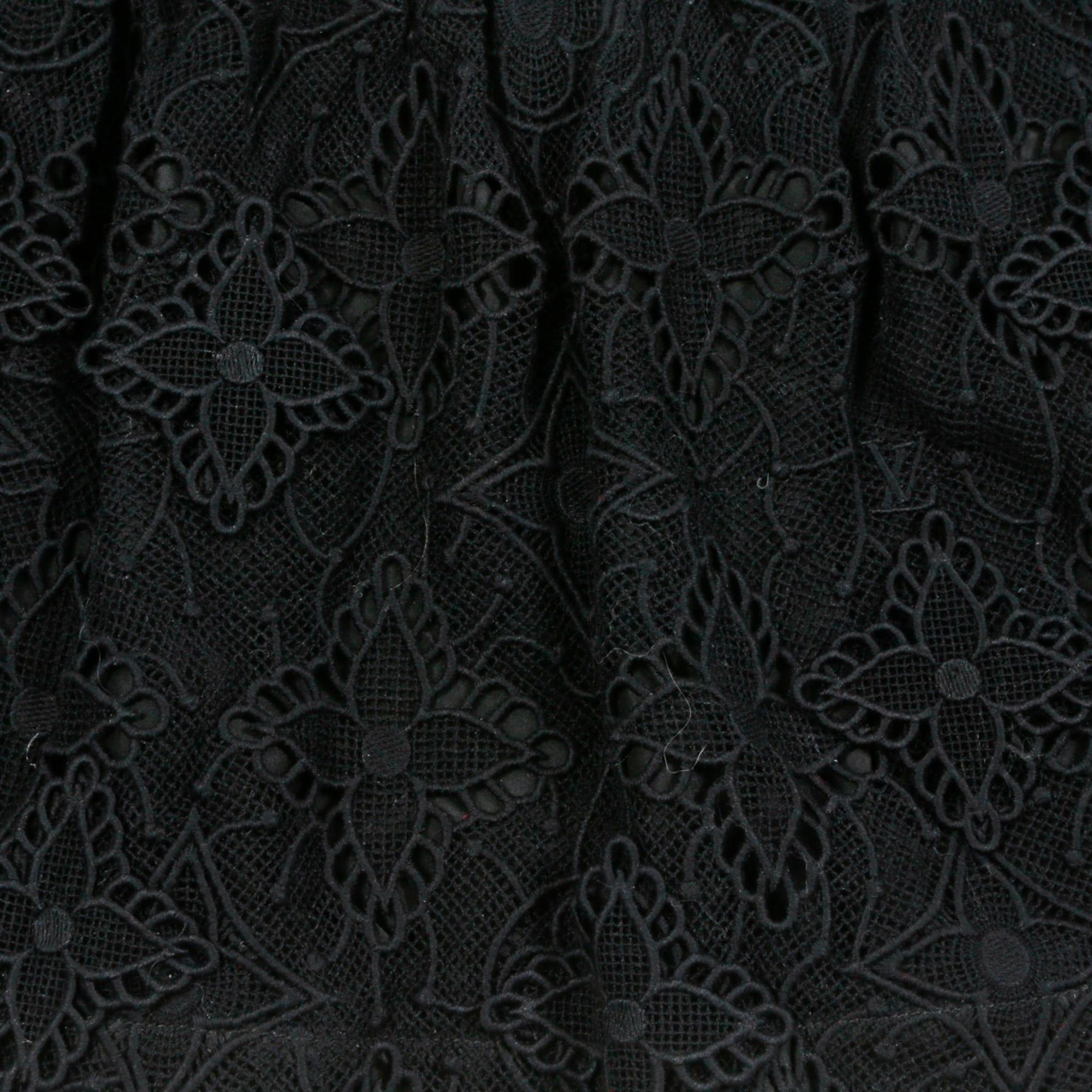 Jupe courte Louis Vuitton en guipure de coton noir avec les symboles iconiques de la marque sur le devant et en crêpe de soie noir au dos, doublure en toile de satin noir, taille légèrement élastiquée, fermeture zippée contrastante au dos. Taille