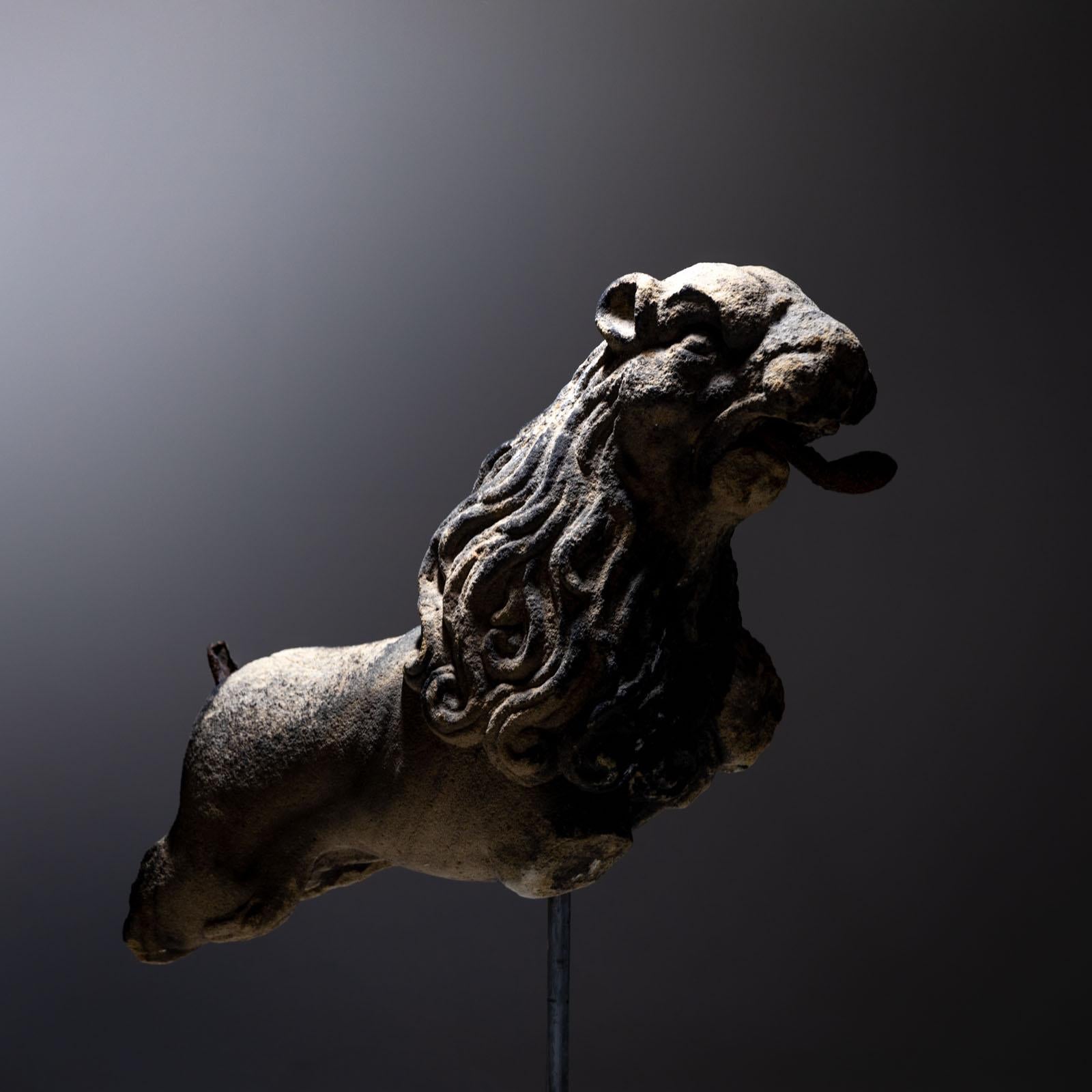Sculpture of a lion preserved in fragmentary condition with curved iron tongue and long mane. The iron tail is still present as a remnant. There is an iron ring on the back. The lion was subsequently mounted on a three-pass sandstone base with an