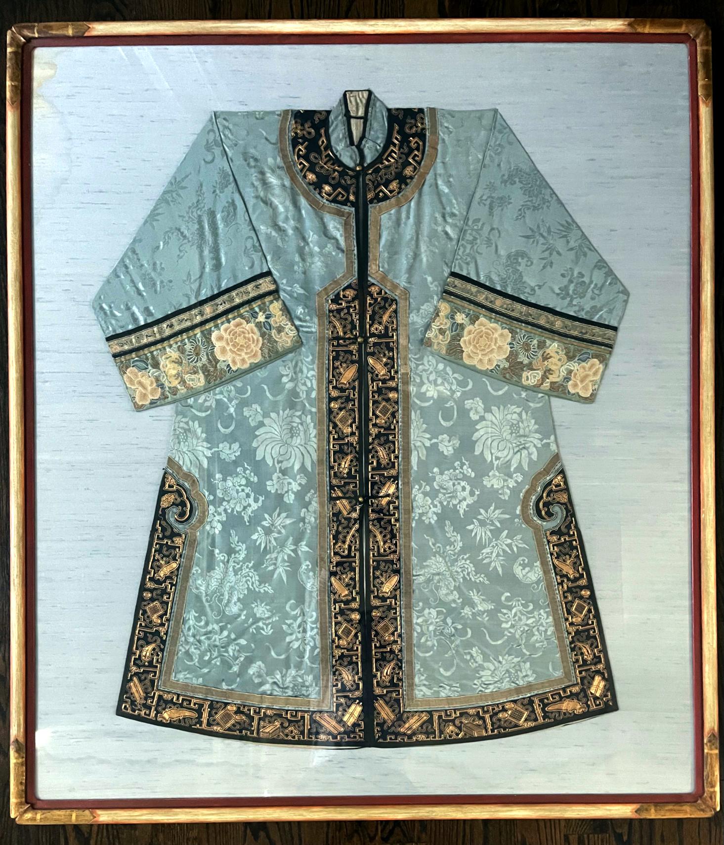 A woman's coat made of blue woven brocade with wide sleeves from China late Qing Dynasty (circa mid to late 19th century), professionally mounted and presented on blue linen board and framed as a beautiful piece of textile art. The coat features