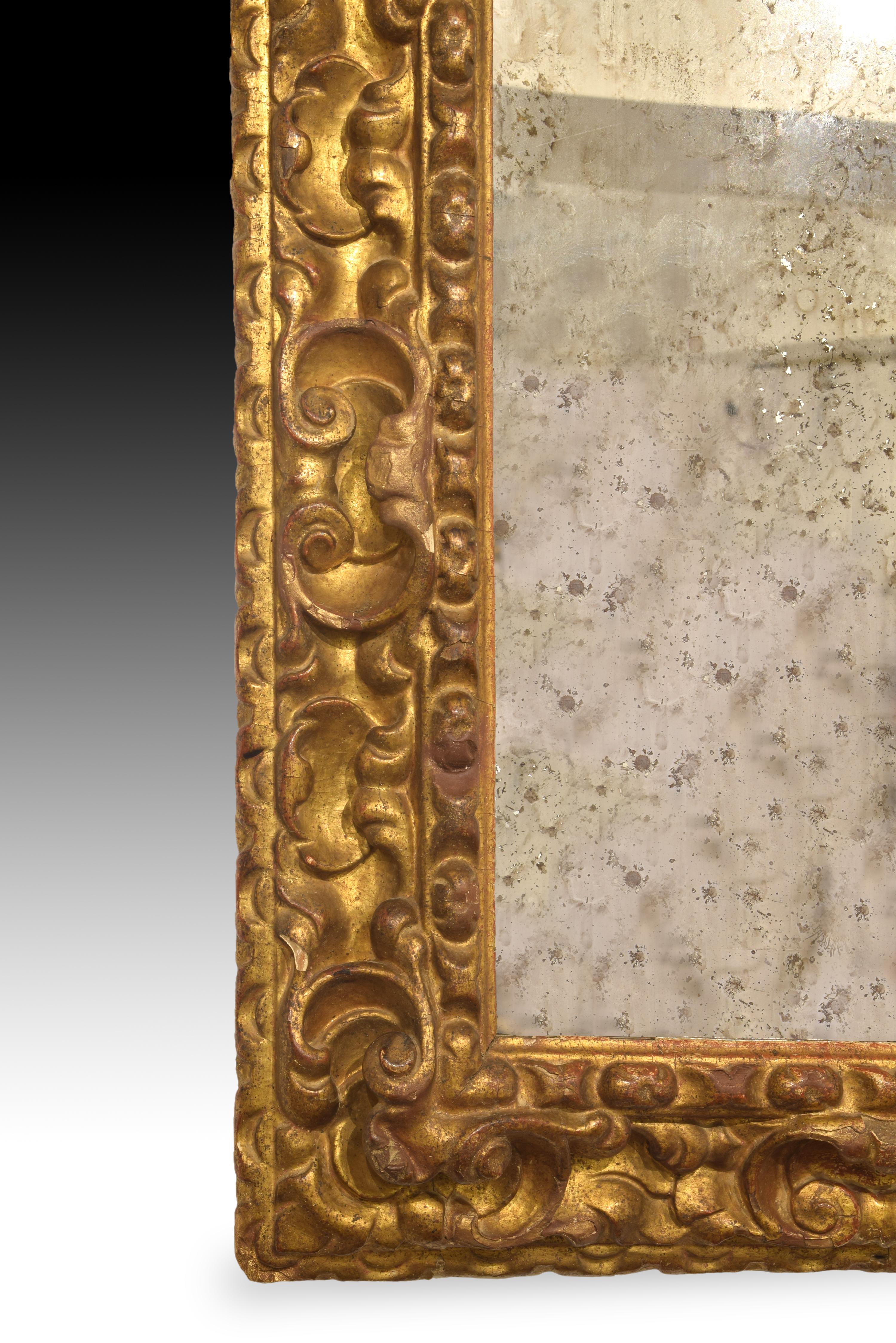 Rectangular mirror with carved and gilded wooden frame which presents some sizes distributed in bands. A slightly wavy outer edge already advances the predominance of the curves of the piece; to the center a wider area worked with scrolls 