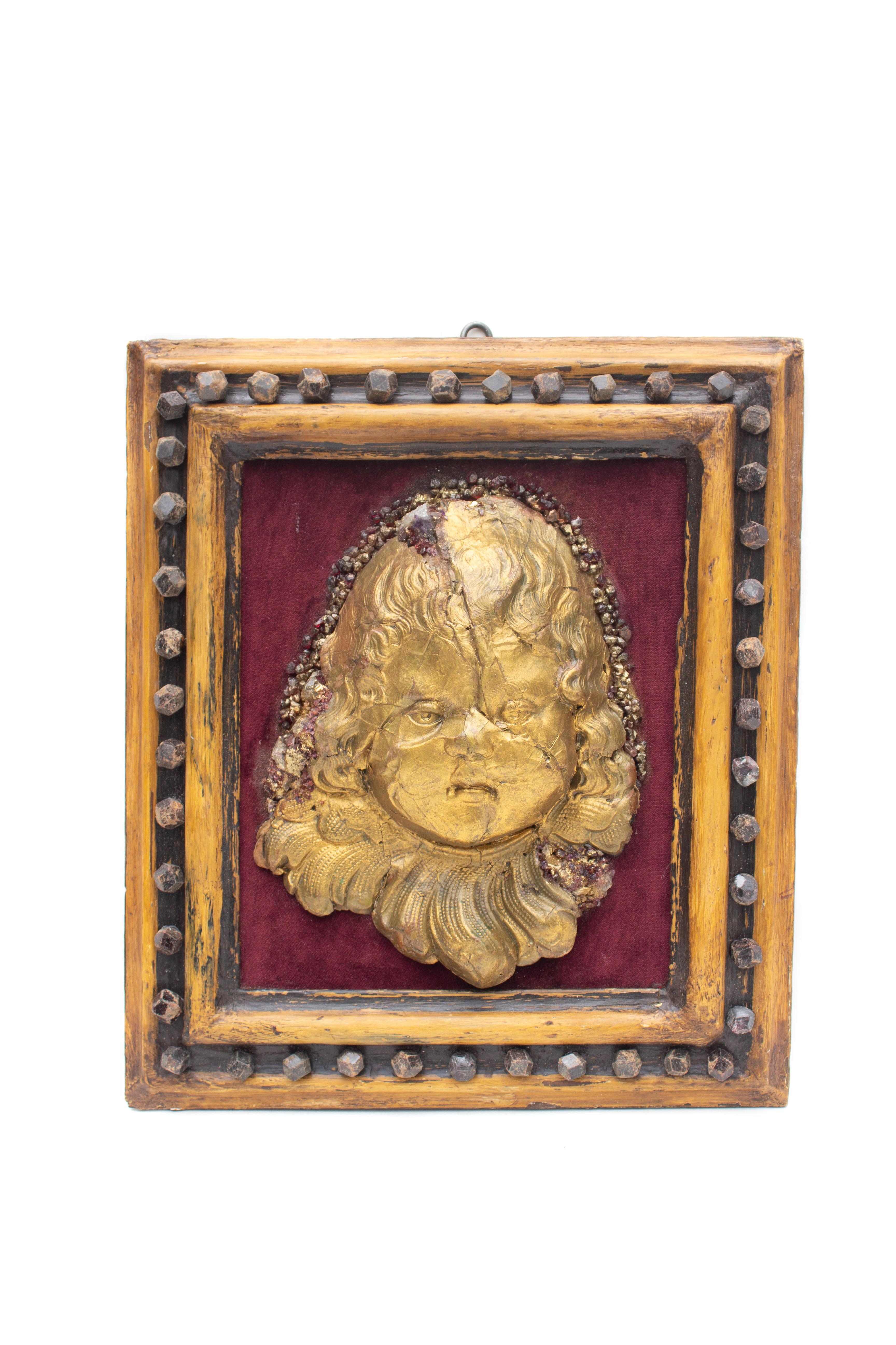 Framed 18th century Italian gold leaf angel head 'putto' wall relief sculpture with burgundy velvet and adorned with rubies and garnets. There is a halo of rubies and garnets around the head and the angel 'putto' was sculpted from papier-mâché. It