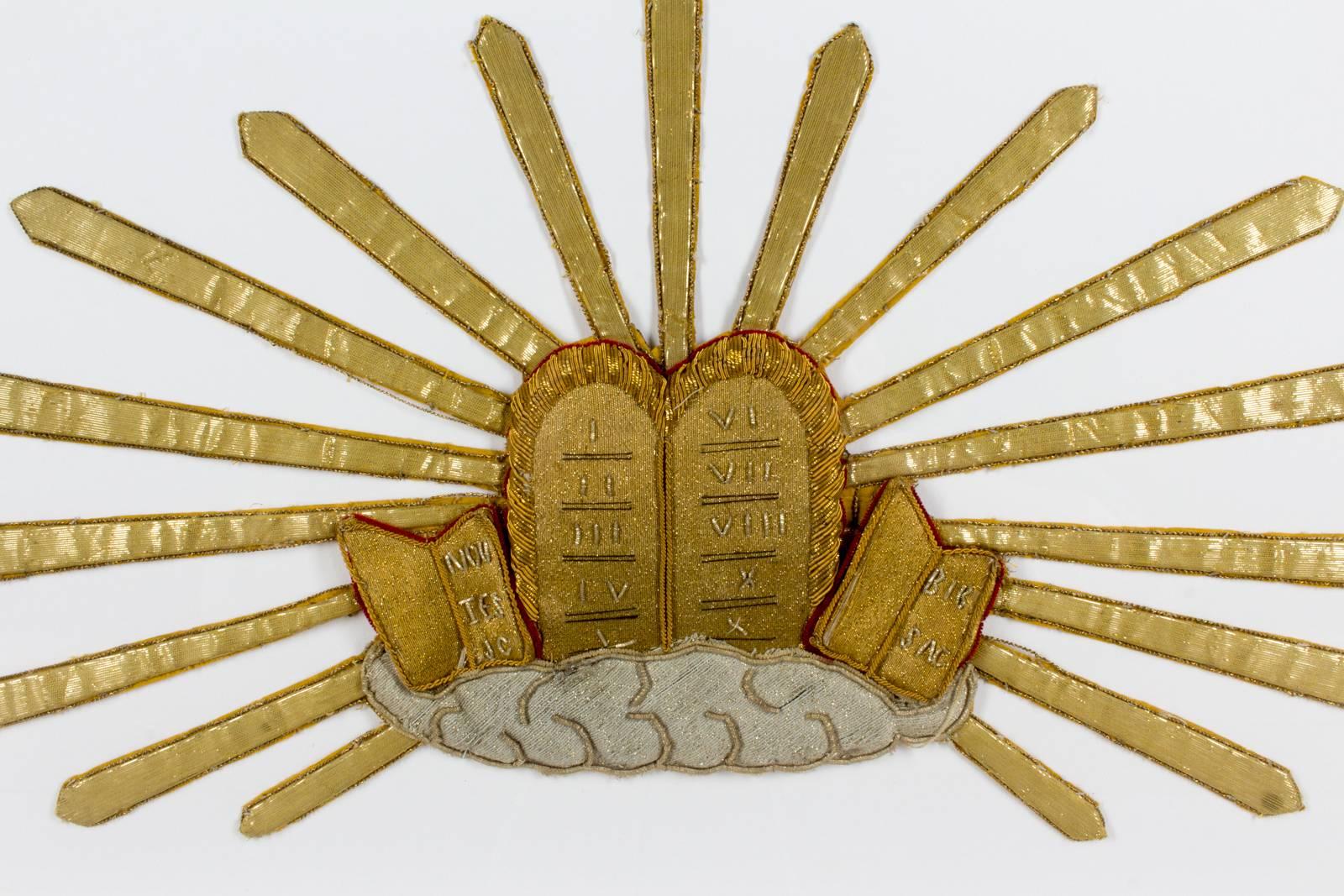 This beautifully made antique (late 1800s) textile fragment features an embroidered image of the Ten Commandments surrounded by light. The embroidery is not flat, but rather three-dimensional. We believe this particular fragment was once worn on the