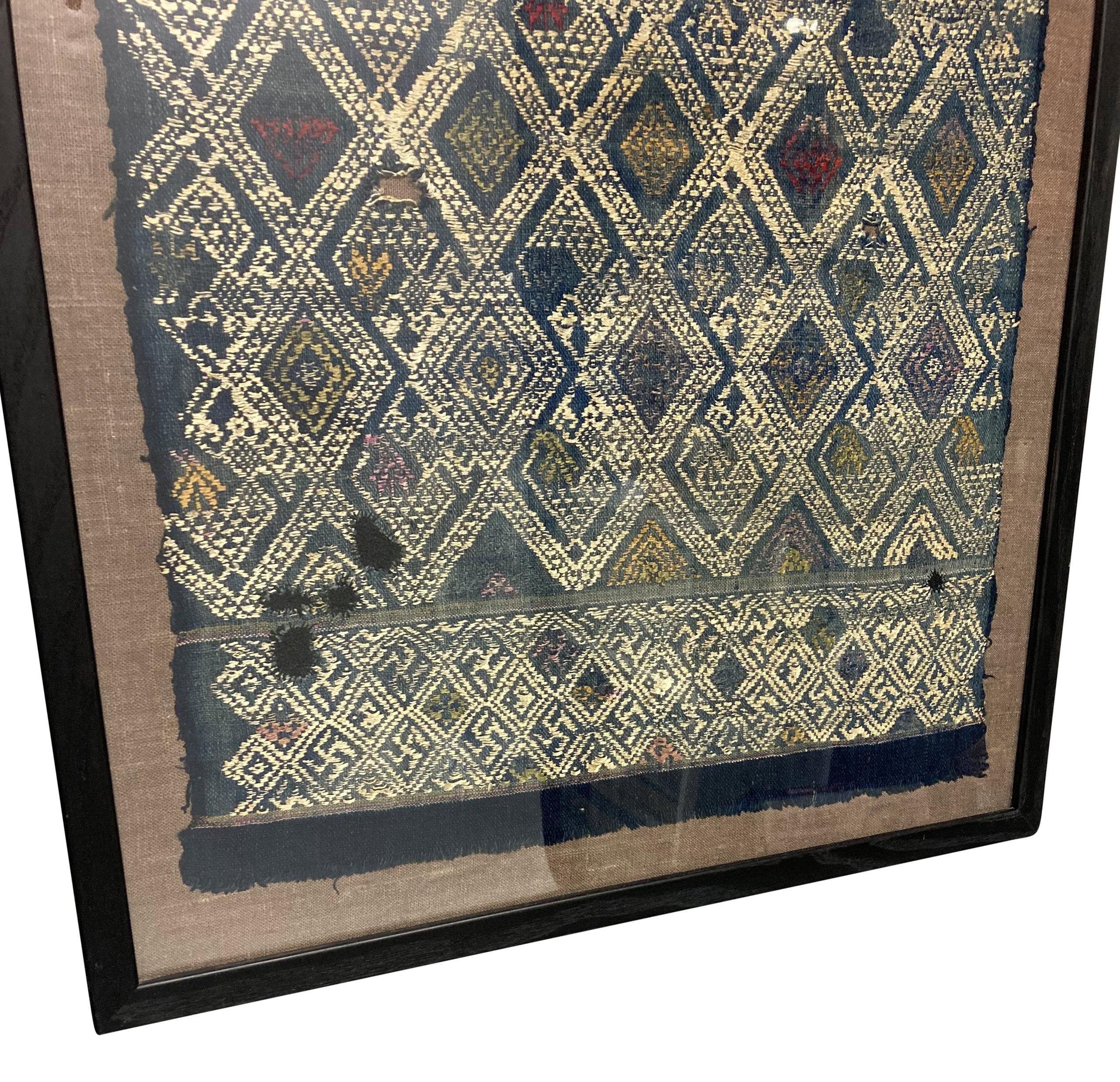 A Chinese, traditional hand-woven textile from the southwestern Guiqzou Province. Framed behind glass, against a raw linen background.