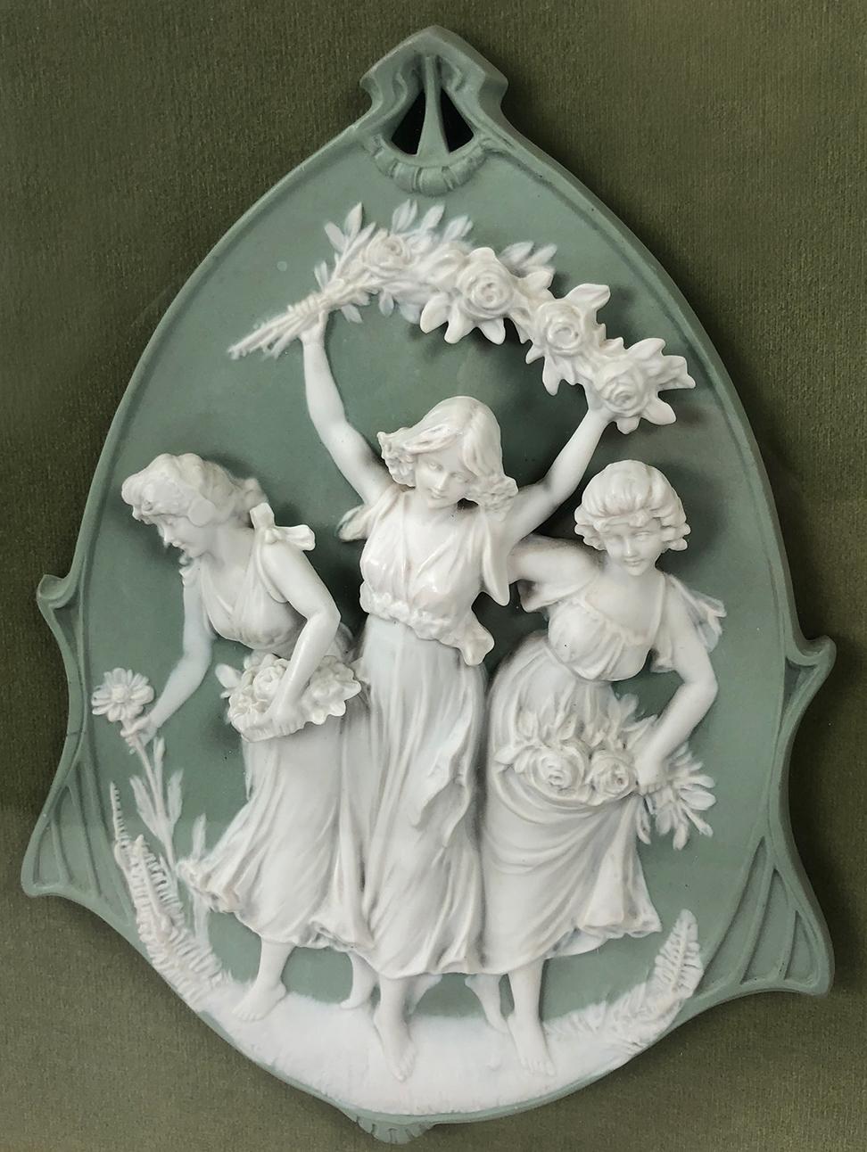 A framed biscuit porcelain Jasperware relief cameo with three women dancing and picking flowers. Likely an 18th / 19th century German wedgwood-like jasperware piece. This piece is framed in a glass floating frame on top of sage green felt. A small