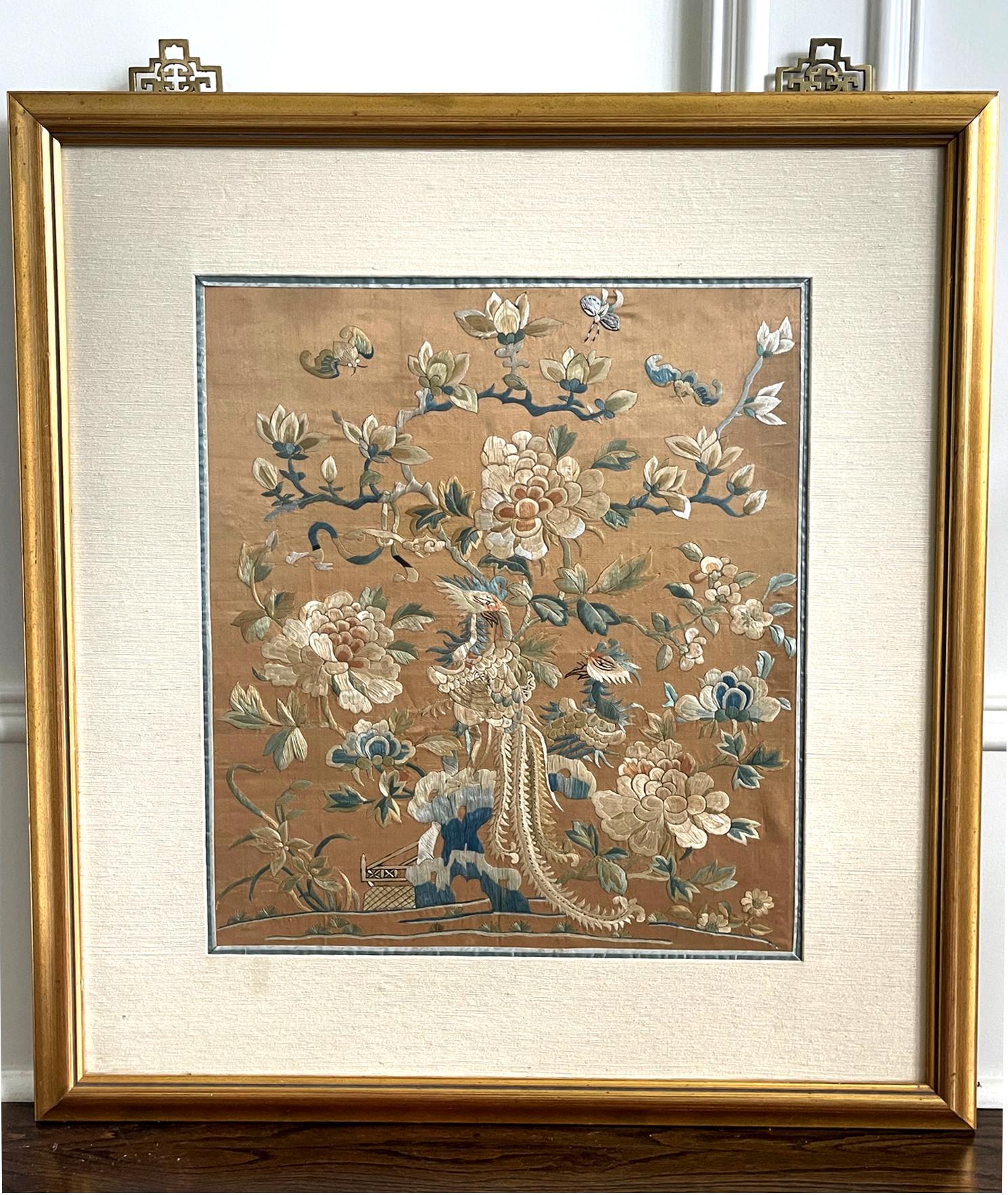 A Chinese silk panel with elaborate embroidery circa late 19th century, end of Qing Dynasty. On the salmon pink background, the image depicts a pair of phoenixes perched on rocks surrounded by blooming peonies with butterflies and bats flying around