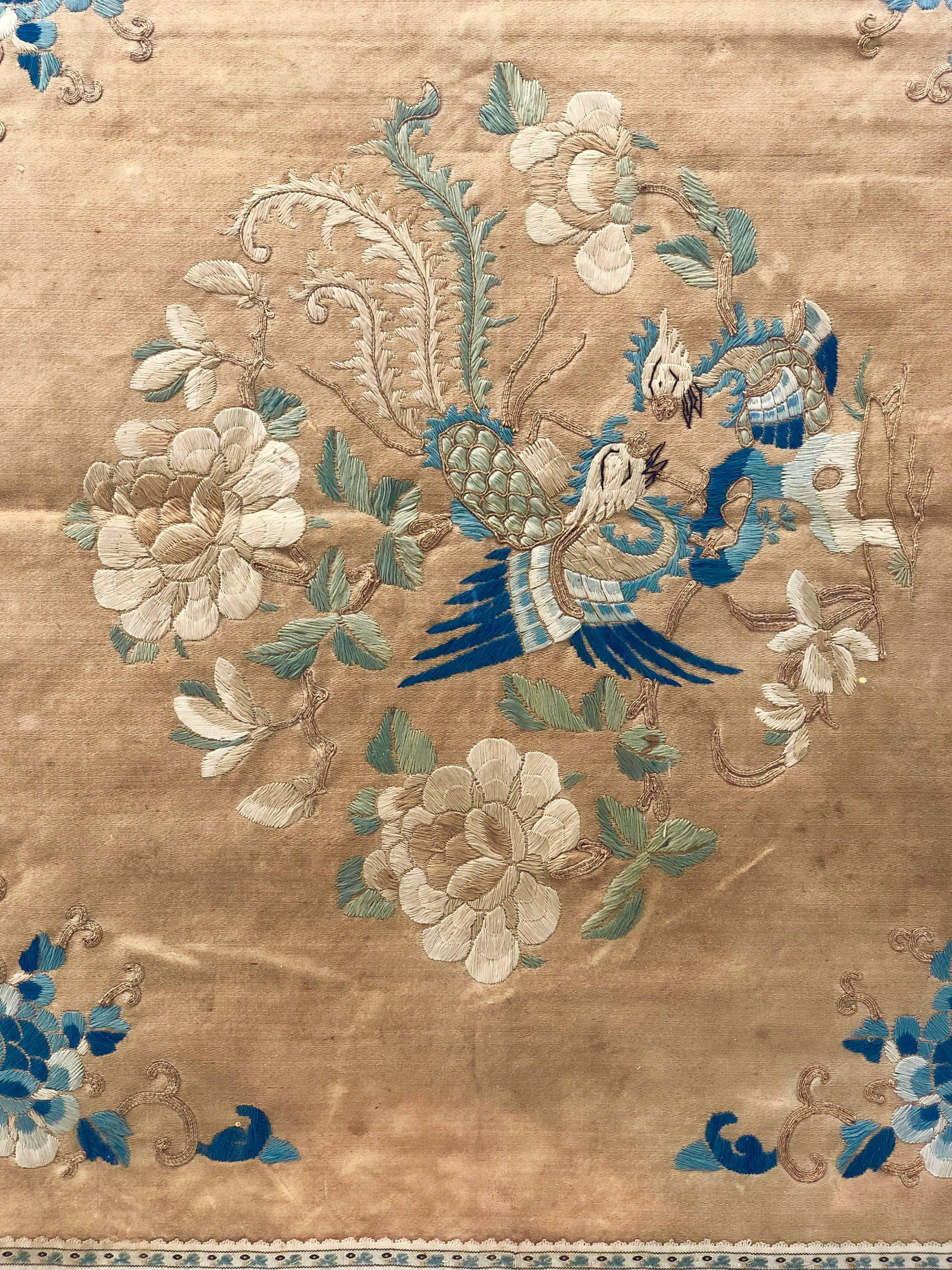 This beautiful framed Chinese silk embroidery shows two birds in a variety of beautiful blue colors with green leaves and cream colored flowers on the center circle and blue and cream colored flowers on the four corners. All are embroidered on a
