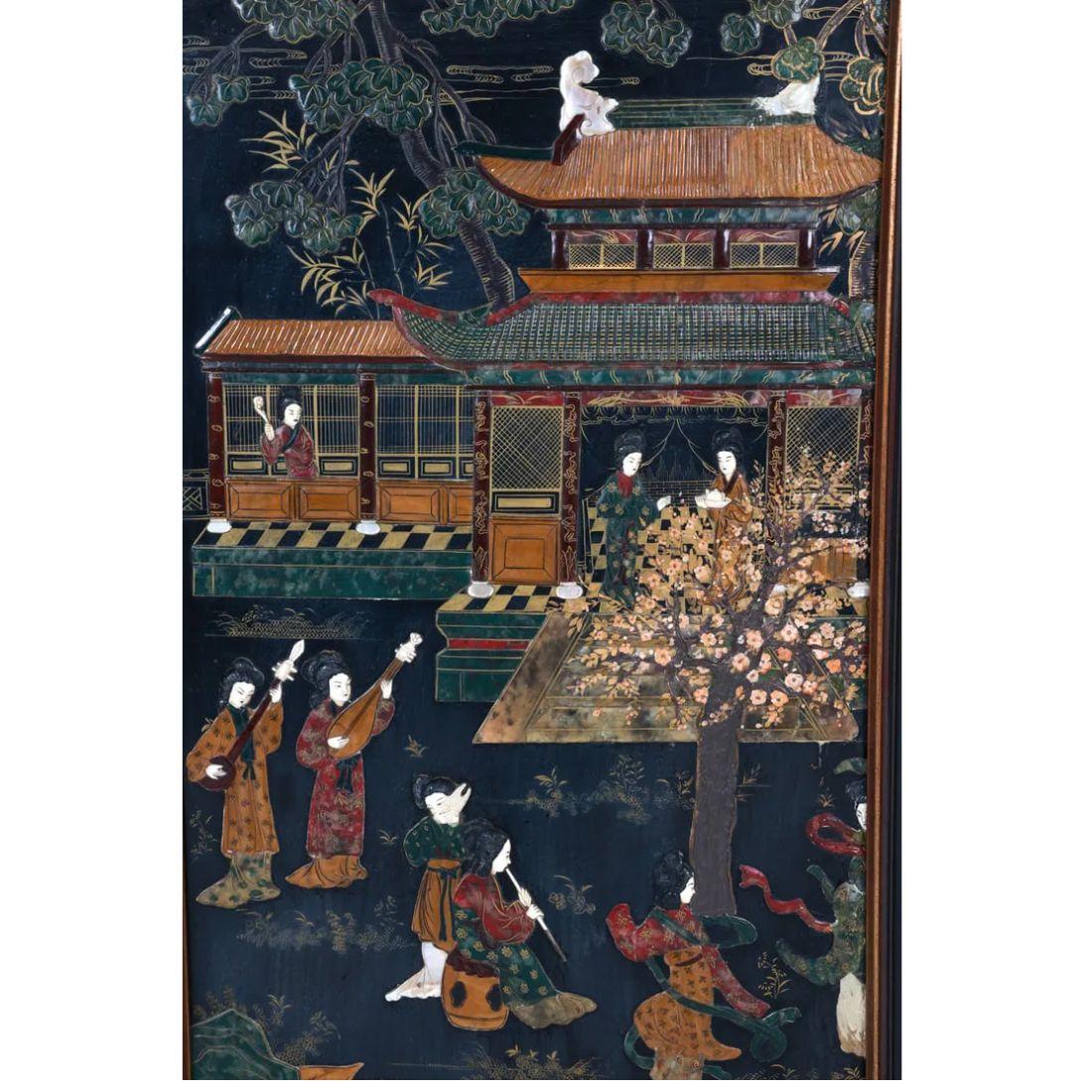 This captivating framed Asian panel showcases a masterful enamel and stone inlay on wood, depicting a serene outdoor scene of women playing musical instruments. The women are gracefully positioned in front of a traditional pagoda, with a large tree