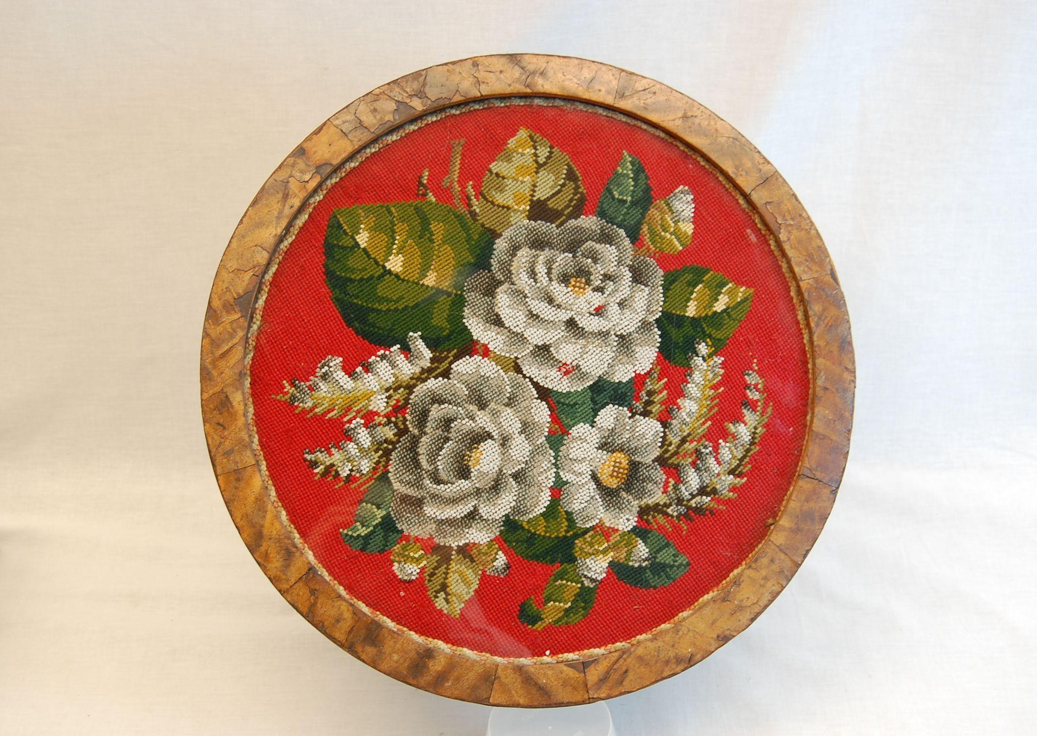 A circular floral needlepoint with clear and colored glass beads mounted in its original wooden frame under glass. It has been mounted onto a later made base, this could always be removed and used as a wall hung circular frame. Needlepoint is in