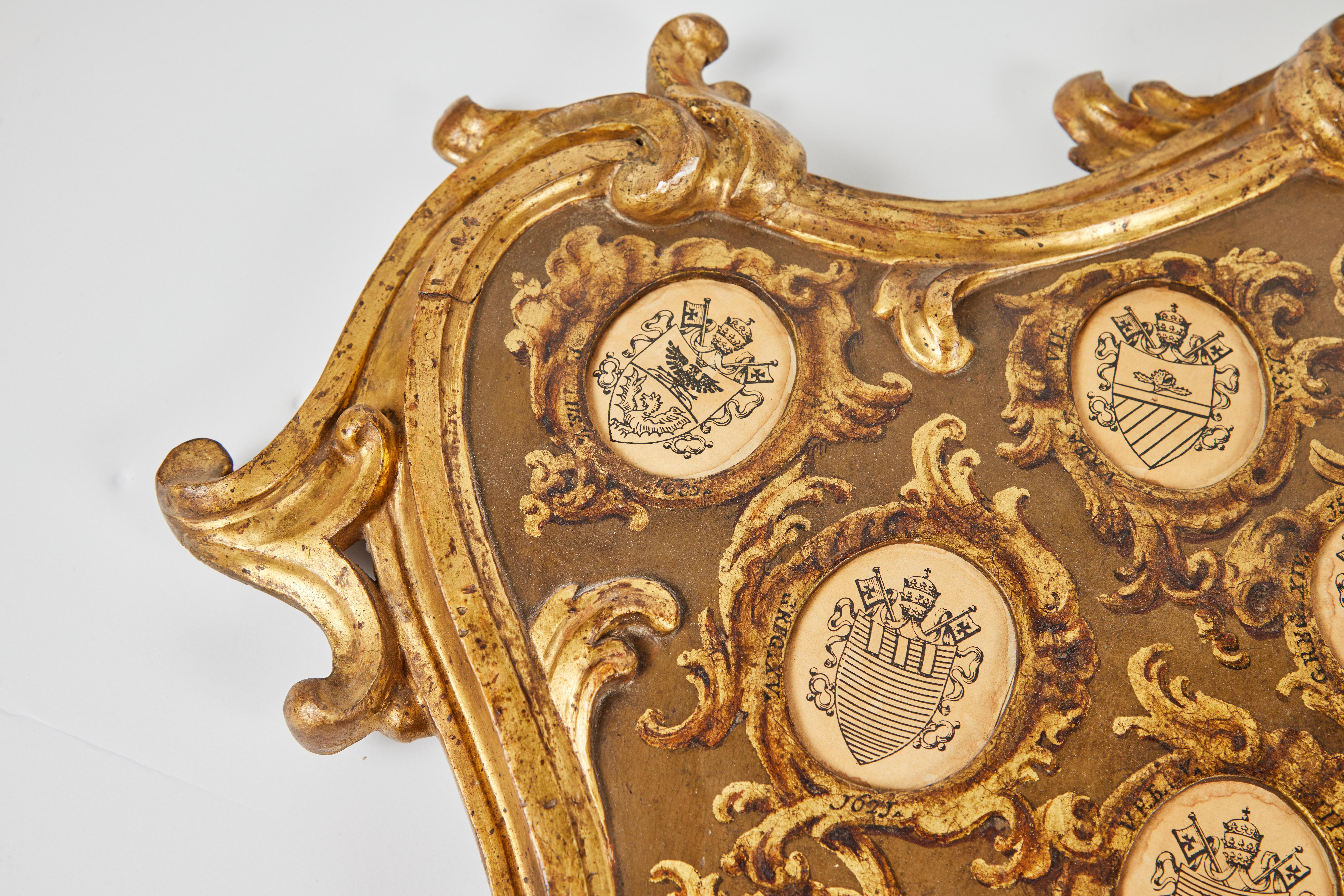 A remarkable, one-of-a-kind, hand-carved, gessoed, 22k gold gilded, hand-painted, foliate embellished serpentine, crest-form, 19th century, convex Italian frame inset with ink-on-vellum images of 24 papal crests. The full set wasn't completed by the