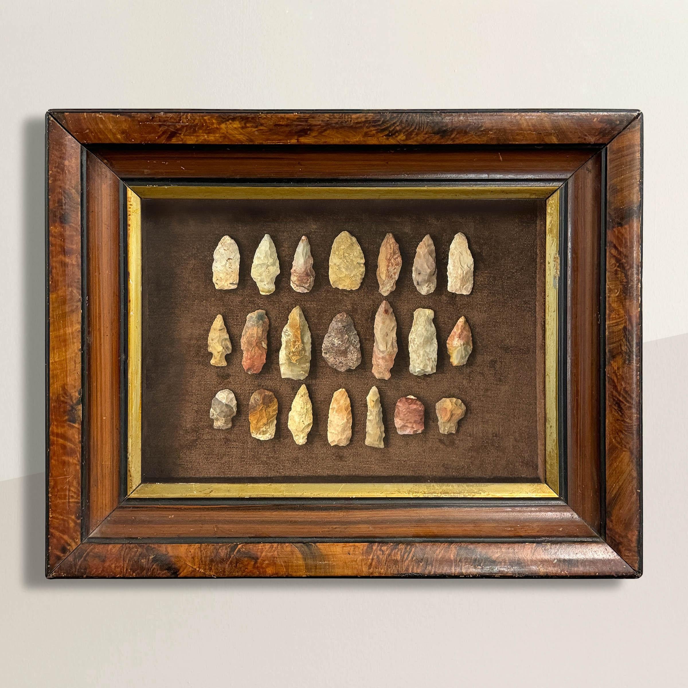 Ein außergewöhnlicher Satz von einundzwanzig Pfeilspitzen aus Stein, die in Waukesha County in Wisconsin gefunden wurden und in einer Schattenbox aus dem 19. Jahrhundert mit Kunstmalerei eingefasst sind, fängt nicht nur die Schönheit ihrer