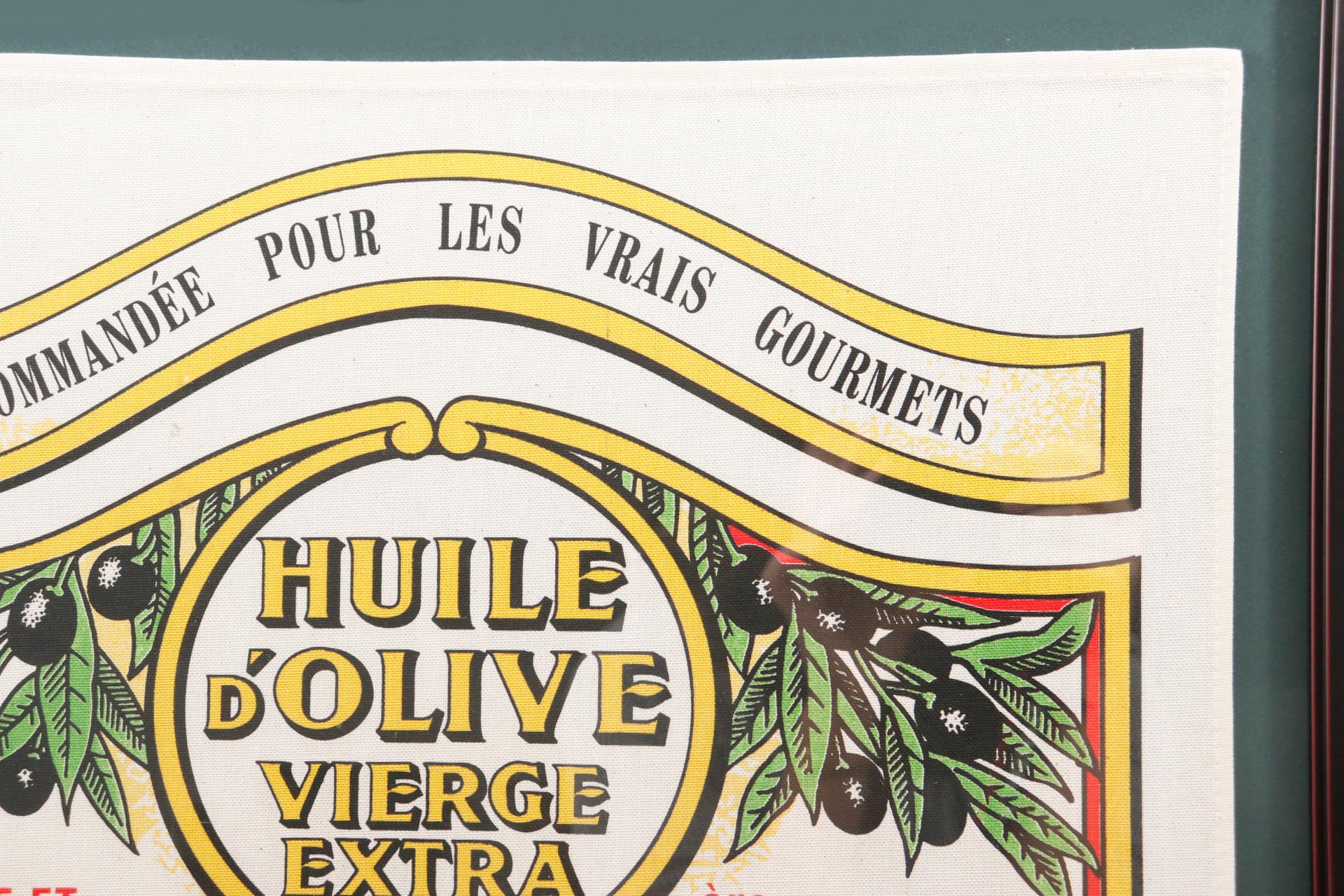 Ein gerahmtes französisches Geschirrtuch aus Baumwolle, verziert mit einem alten Nicolas Alziari Huile d'Olive-Etikett. Maison Alziari stellt seit 1868 in Nizza, Frankreich, Olivenöl her.