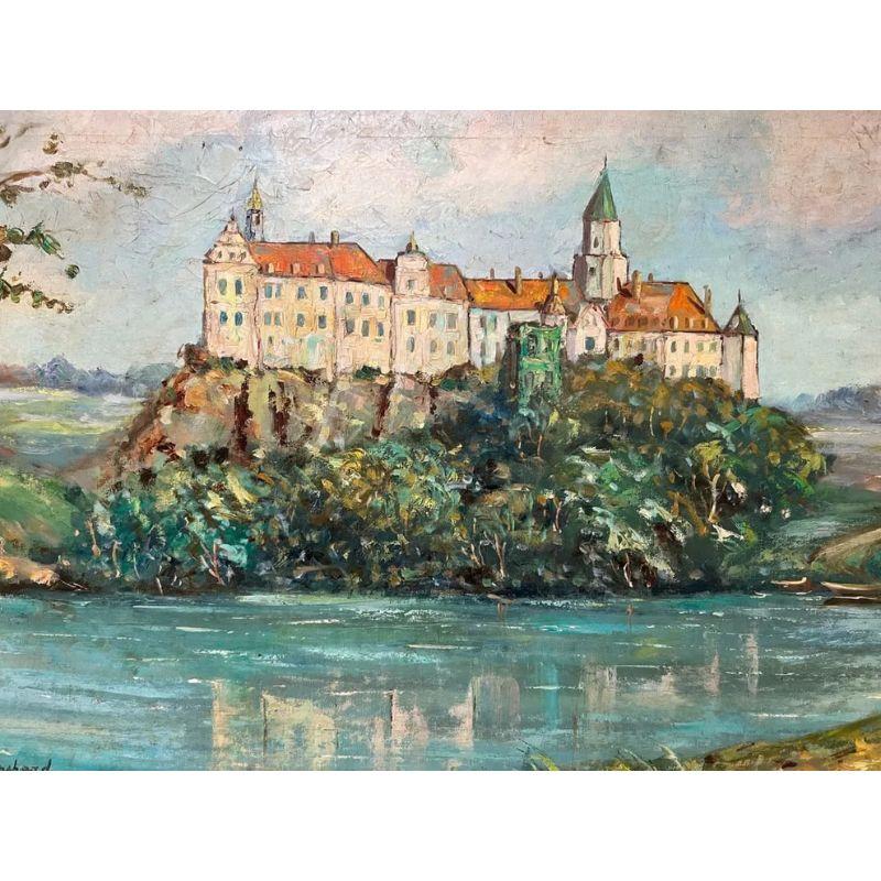 A framed oil on canvas painting that features a red roofed white castle on a hill overlooking a cerulean blue river by French artist,  Blanchard.  The castle is visible reflected in the water, adding to the tranquility of the scene.