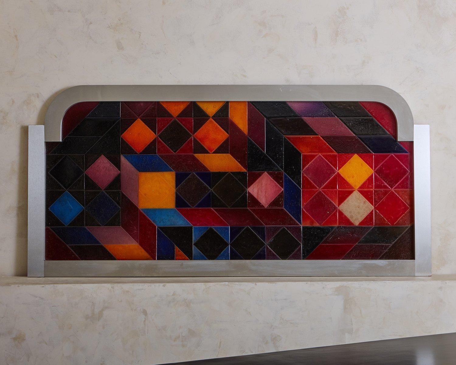 A vintage wall sculpture featuring a resin geometric pattern with rich red, blue and black hues. The piece emulates tile with a beautiful textural finish and depth of color. This piece has a rectangular brushed metal frame with rounded top corners.