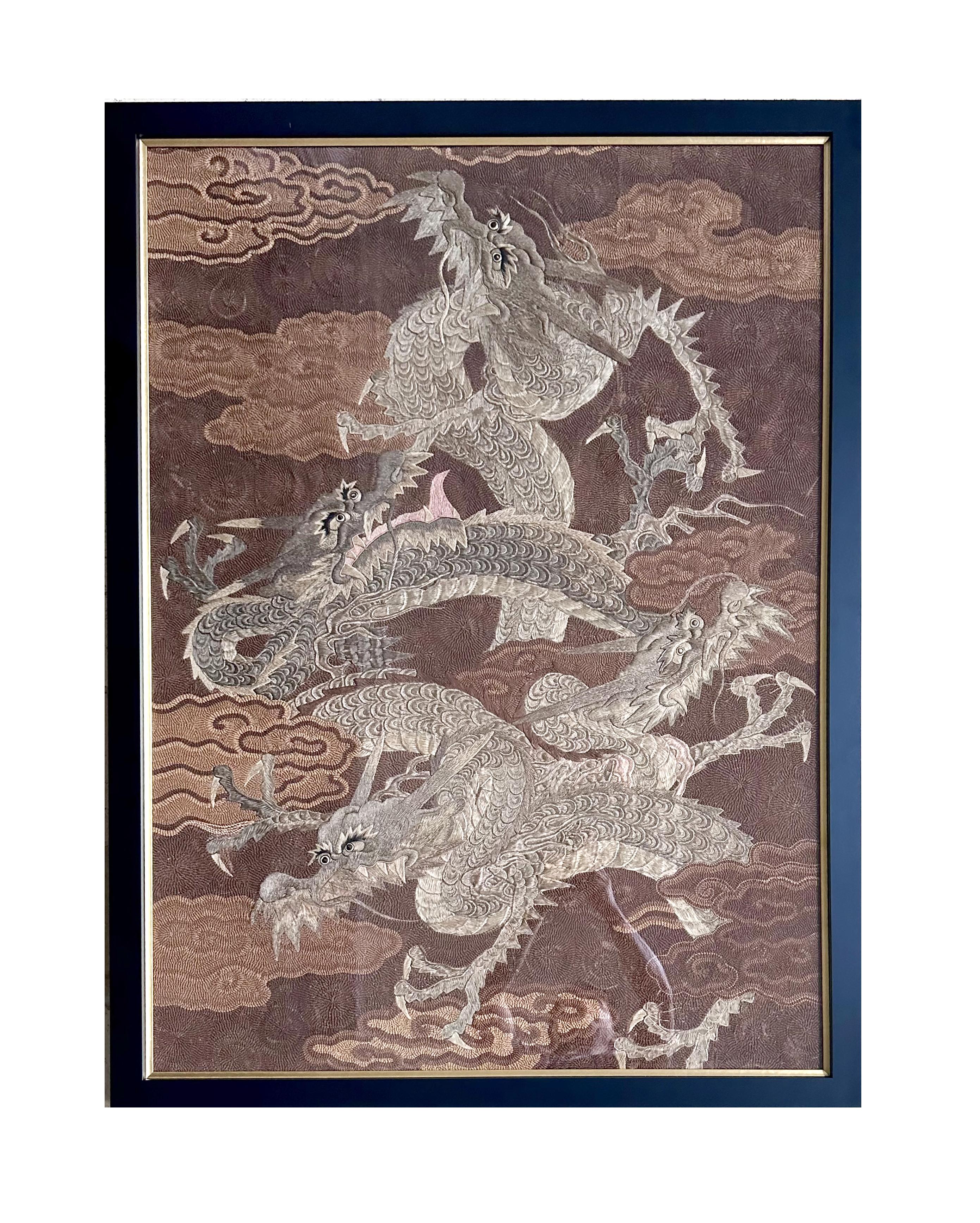 Un llamativo tapiz bordado japonés de hacia la década de 1890, periodo Meiji, presentado en un marco de madera dorada bajo vidriado. El diseño presenta cuatro dragones enroscados y deslizándose entre las nubes. El dragón, la criatura mitológica más