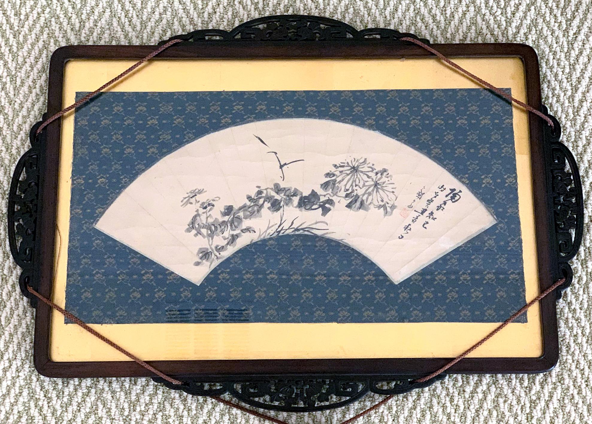 An ink painting on the fan surface by Japanese Zen artist Hidaka Tetsuo (1791-1871), now framed in a traditional Japanese carved wood frame with silk fabric mat and decorative hanging tassels. The painting depicts a floral group consisting of autumn