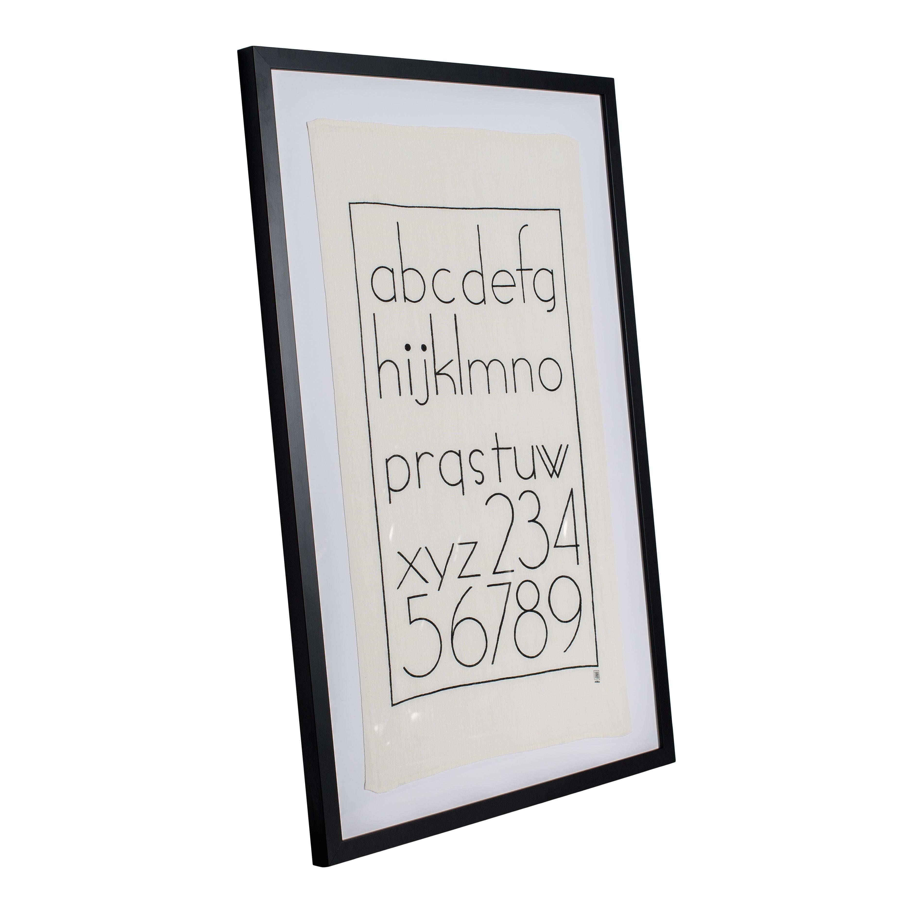A simple framed print on linen that contains the alphabet and numbers 2-9. The black frame is simple and sleek and features a white matt with the linen print on top. The letters and numbers are printed on a slightly off-white piece of linen in black