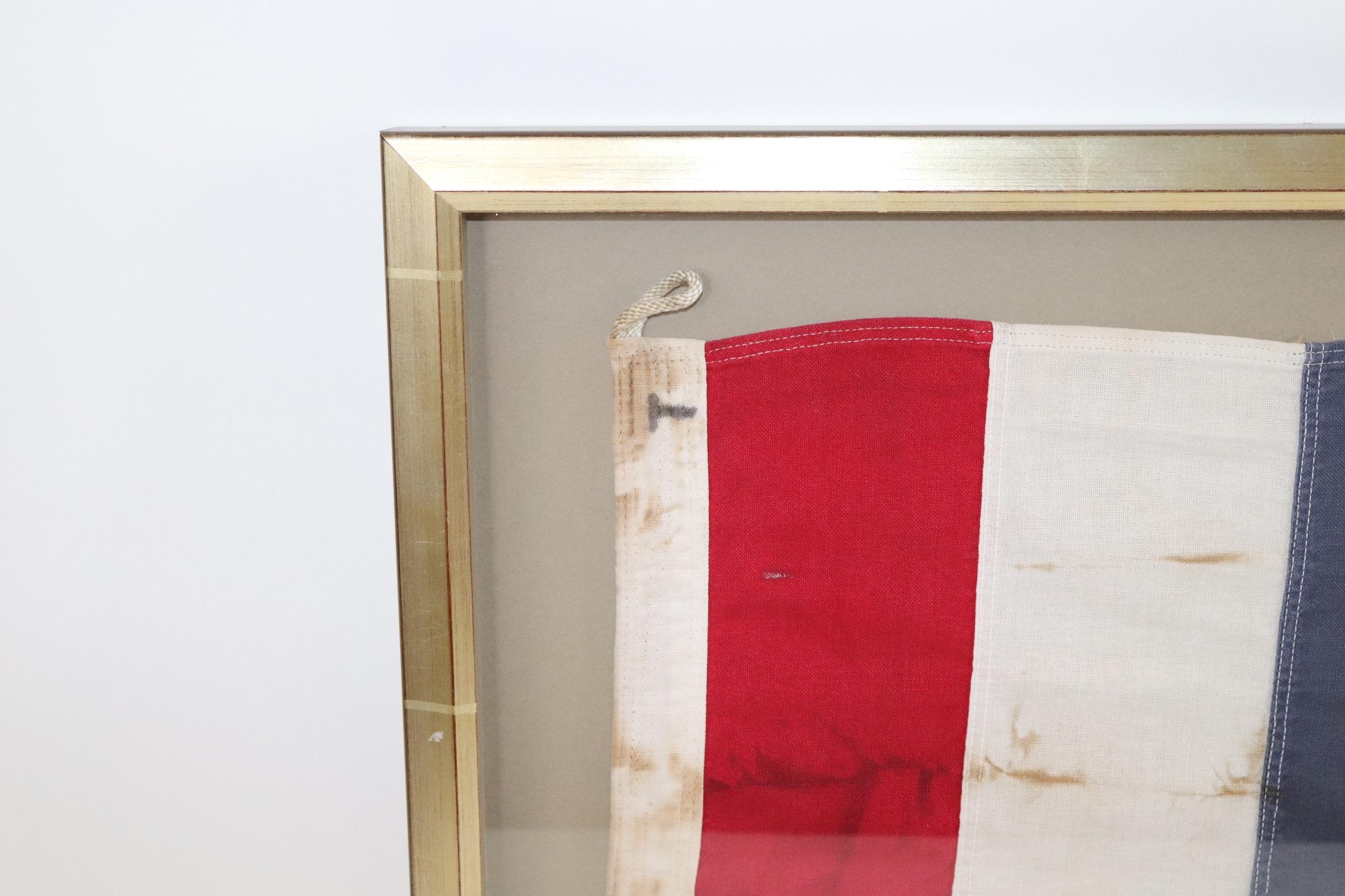 Shadow box framed signal flag with attached rope and wood toggle. Red, white and blue field. Weight is 5 pounds.