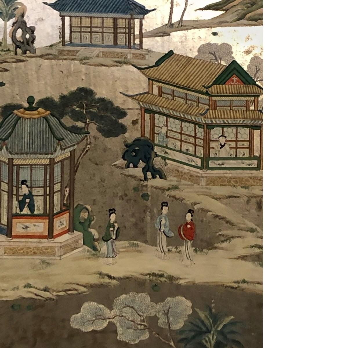 This framed wallpaper panel depicts a serene setting of a Chinese courtyard that is set against a beautiful hill. The metallic wallpaper panel is set against an orange fabric matte that is encased in a silver leaf molded wood frame. This framed