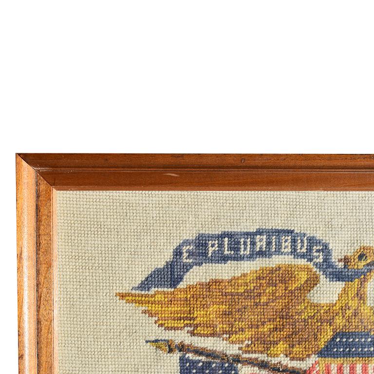 handstitched needlepoint framed American Eagle. Woven from wool, the subject of this patriotic cross-stitched piece features a golden Admiral Eagle with hints of brown. Its wings are outstretched and it's head glances to the side. From his mouth is