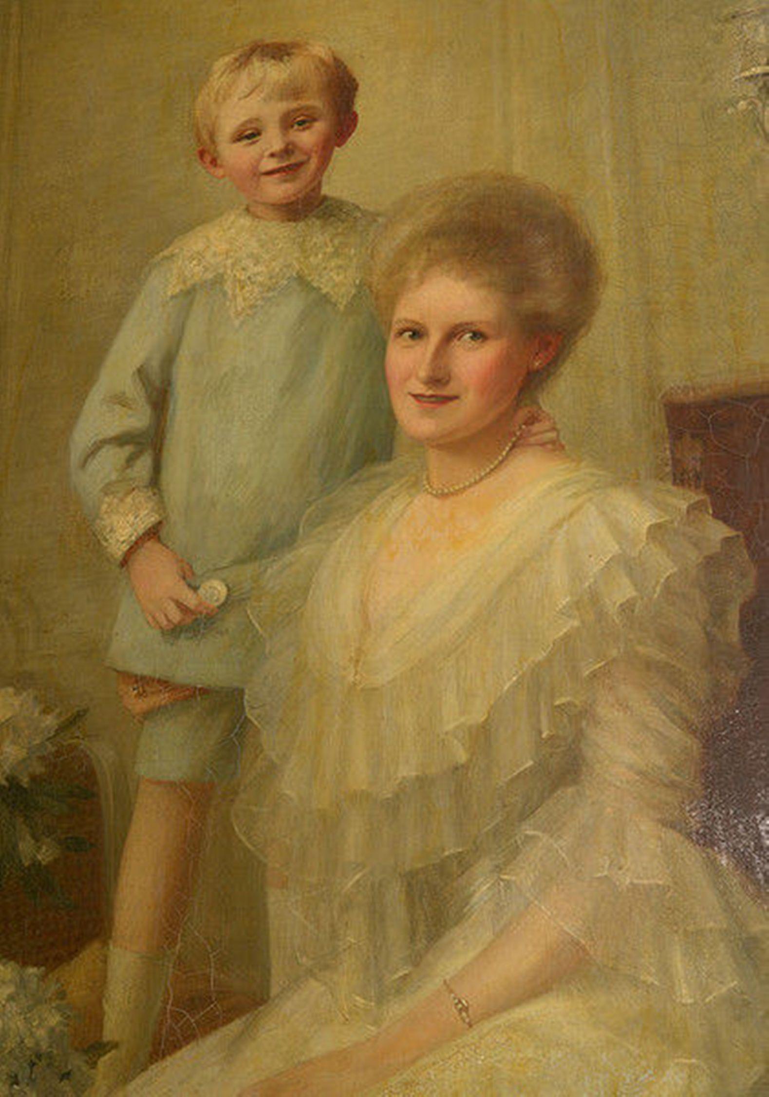 A charming framed Edwardian oil on canvas portrait of a mother and son in a drawing room setting.

The mother seated with her young son standing behind, both beautifully attired.

A mahogany cabinet bearing a silver candelabra sits to the right