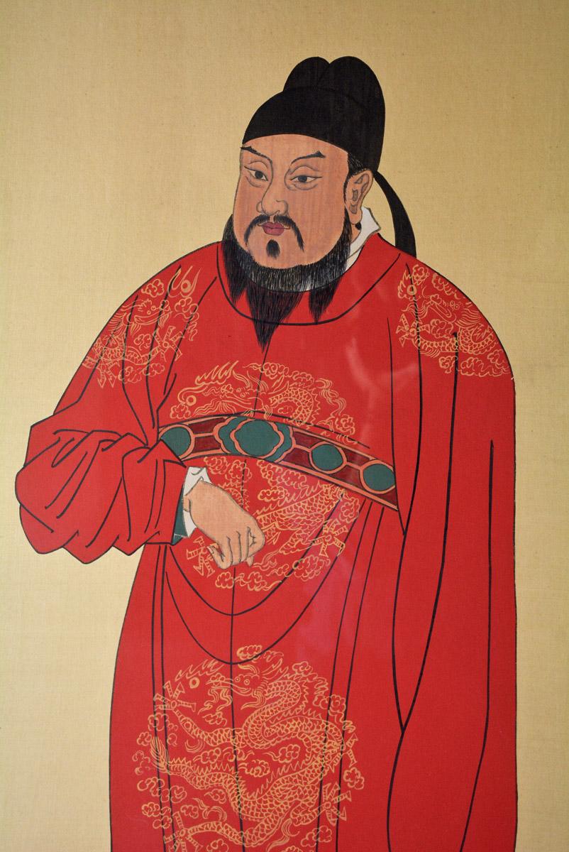 The black-framed print (under glass) is of a distinguished Chinese ancestor painting of a gentleman who is wearing a red robe embellished with yellow dragon-like figures on the skirt, blouse and shoulders. The print is matted with a self-patterned