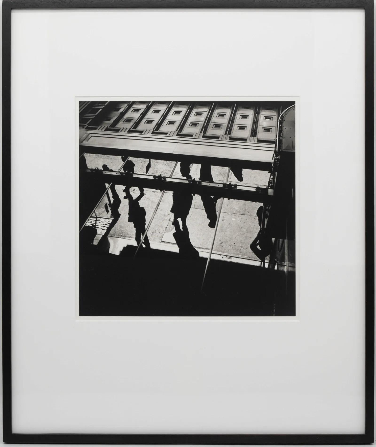 A framed black and white street photograph by Vivian Maier (American, 1926-2009), untitled and undated (circa 1950s), This is a gelatin silver print printed in 2014. This sharply contrasted black and white print captures a street view from a high