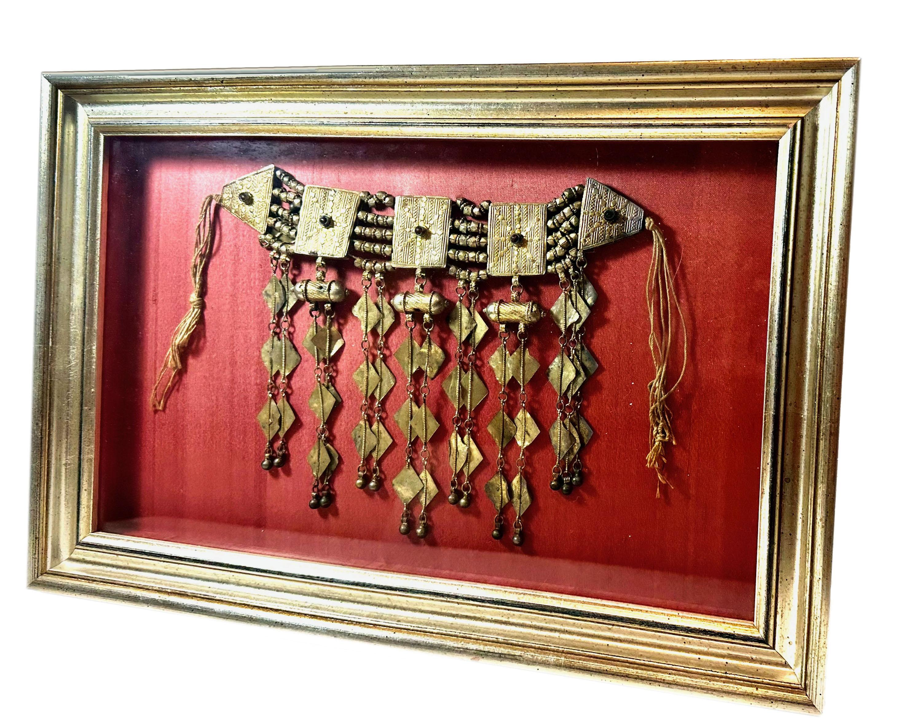A vintage Turkoman ethnic tribal headpiece, beautifully presented in a custom silver gilt frame with a rich pomegranate red background. Originating from Turkey in the early 20th century, this piece embodies the artistry and cultural heritage of the
