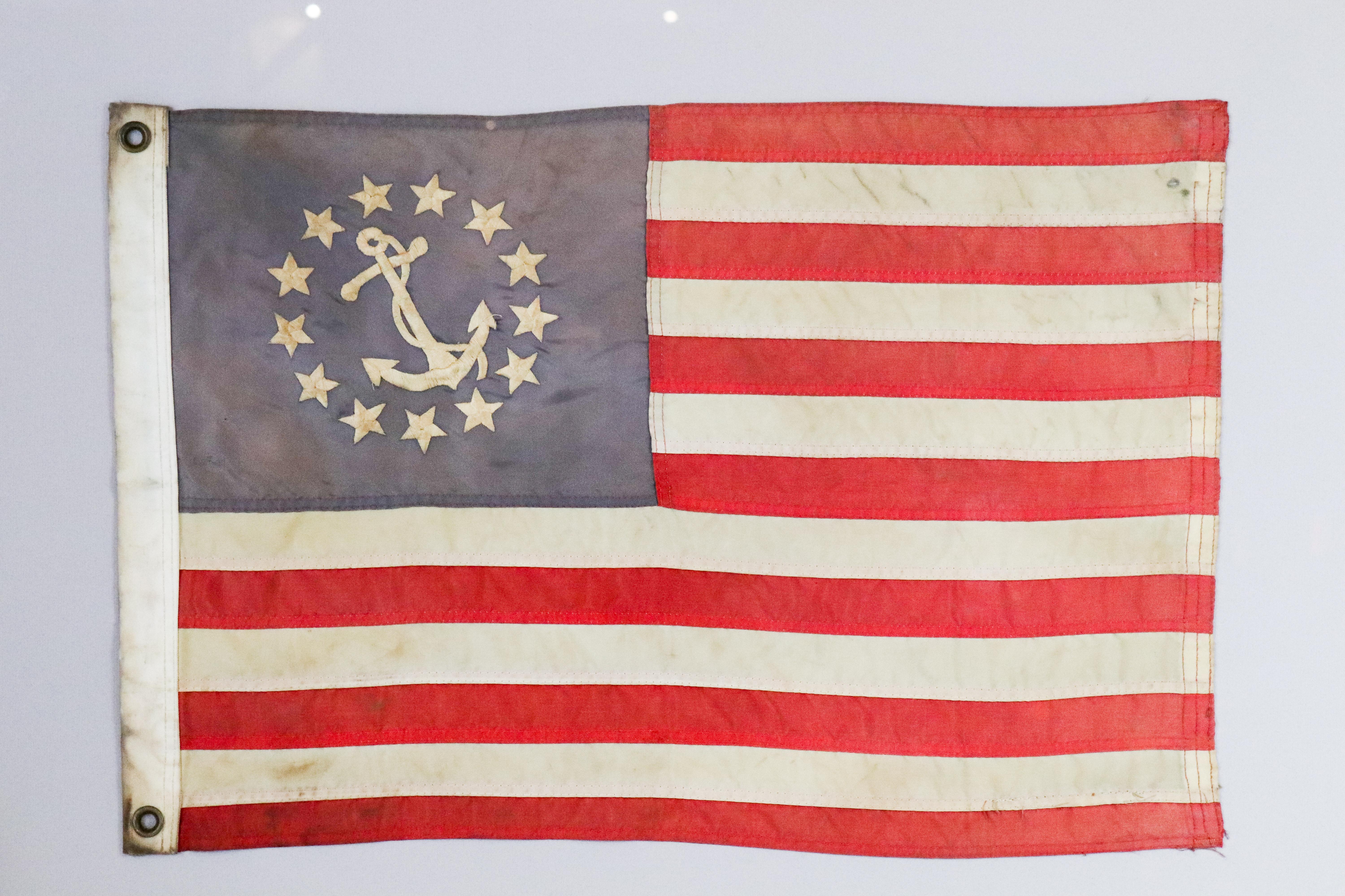American yacht ensign with embroidered fouled anchor and thirteen stars. Hoist with brass grommets. Matted and framed. Measures: 26
