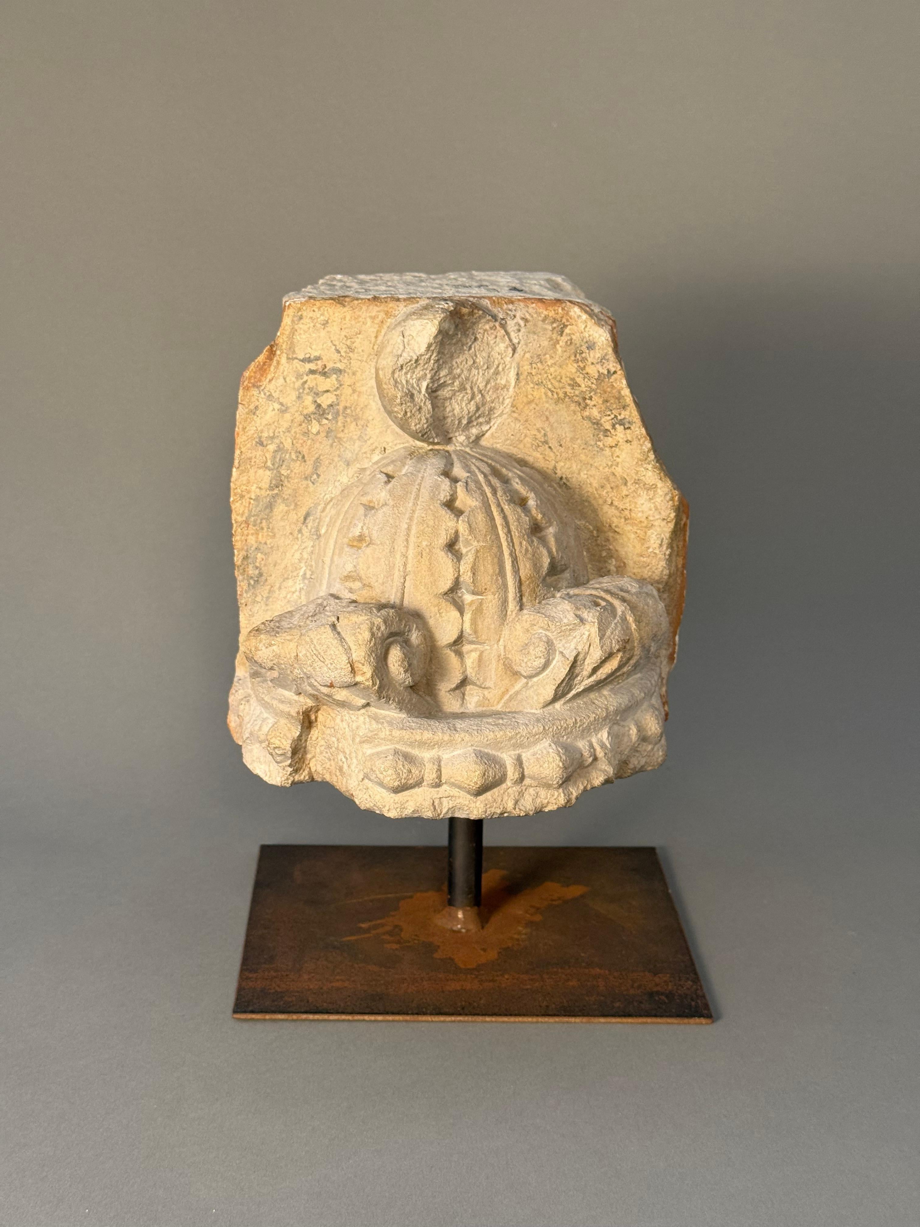 Frammento scultoreo in pietra della seconda metà del XV secolo raffigurante una corona stilizzata scolpita in rilievo, infatti possiamo  notare i segni decorativi tipici delle corone reali, con archi ornati e la parte superiore mancante presentava