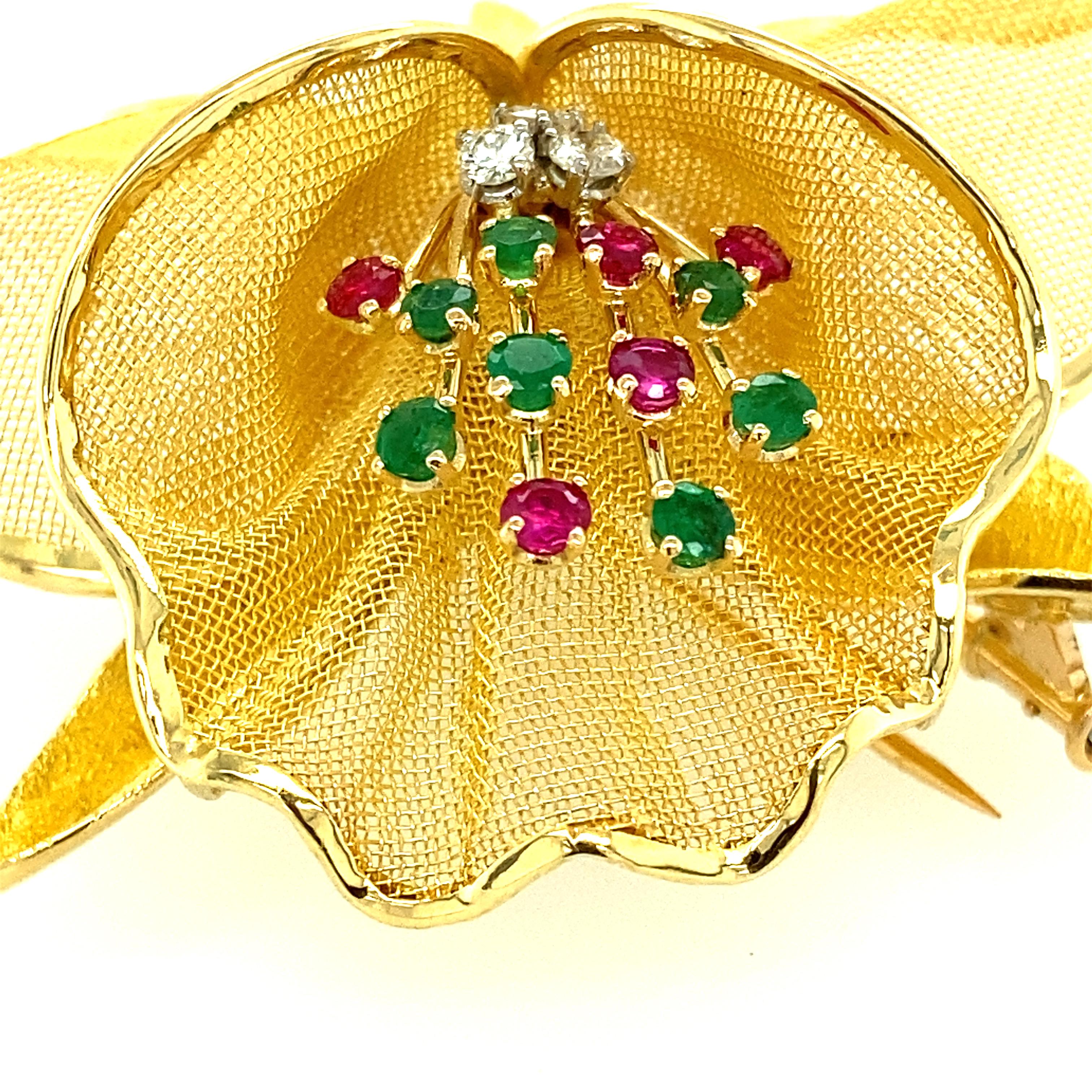 One 18 karat yellow gold (signed Merrin France 18K) orchid design pin set with seven 3mm round emeralds, five 3mm round rubies and three brilliant cut diamonds, approximately I/J color and SI clarity.  The pin measures 2.5 inches in diameter and is
