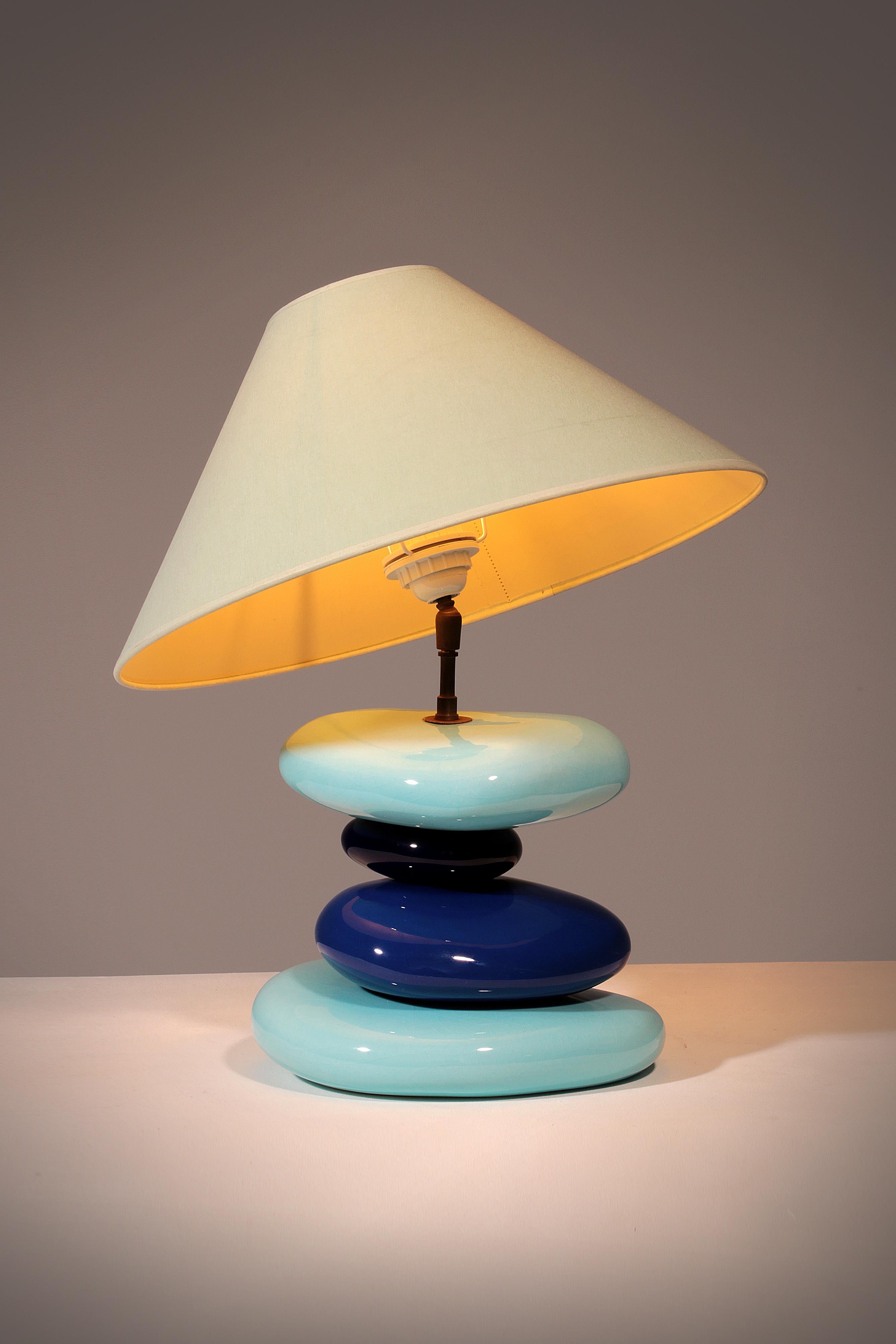 This rare 1980s François Chatain Pebble table lamp is a striking example of French artistic lighting design. Its sculptural base, formed by four handcrafted ceramic pebbles in soft bleu and dark bleu tones, captures the organic elegance that defined