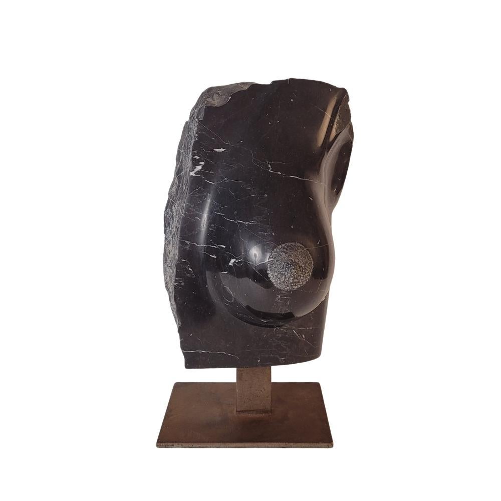 One of a kind  Belgian black marble sculpture on an iron base depicting part of a stylized female torso. What makes this work unique is the contrast between the polished and shiny surface of the front, which offers a soft and serene look, and the