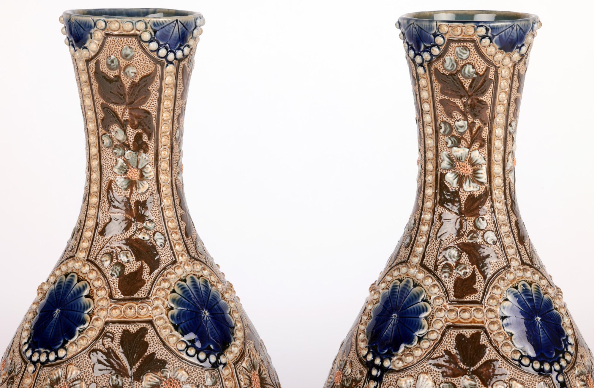 An exceptional and well decorated pair Doulton Lambeth floral vases by renowned artist Frances E Lee and dated 1883. The stoneware bottle shaped vases stand raised on a narrow round foot with slightly recessed bases with pear shaped bodies and