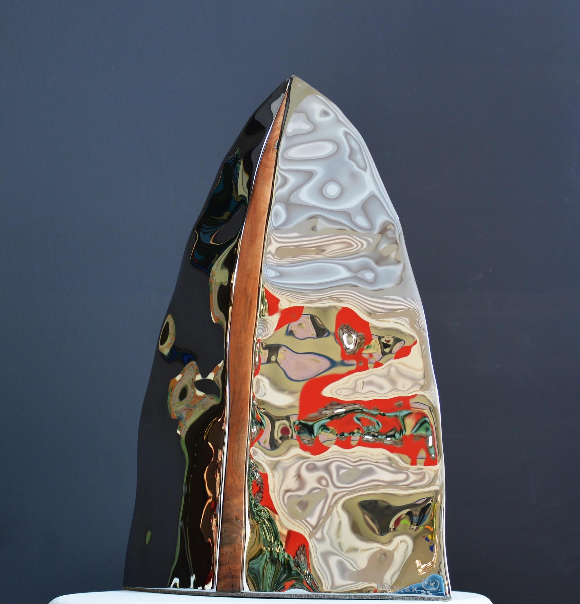 Artefact 1 is a work by the artist Franck K. This work is made of stainless steel and cherry wood.

Franck K’s stainless steel works play with the light and reflections of their surroundings. These sculptures have a perfectly polished surface,