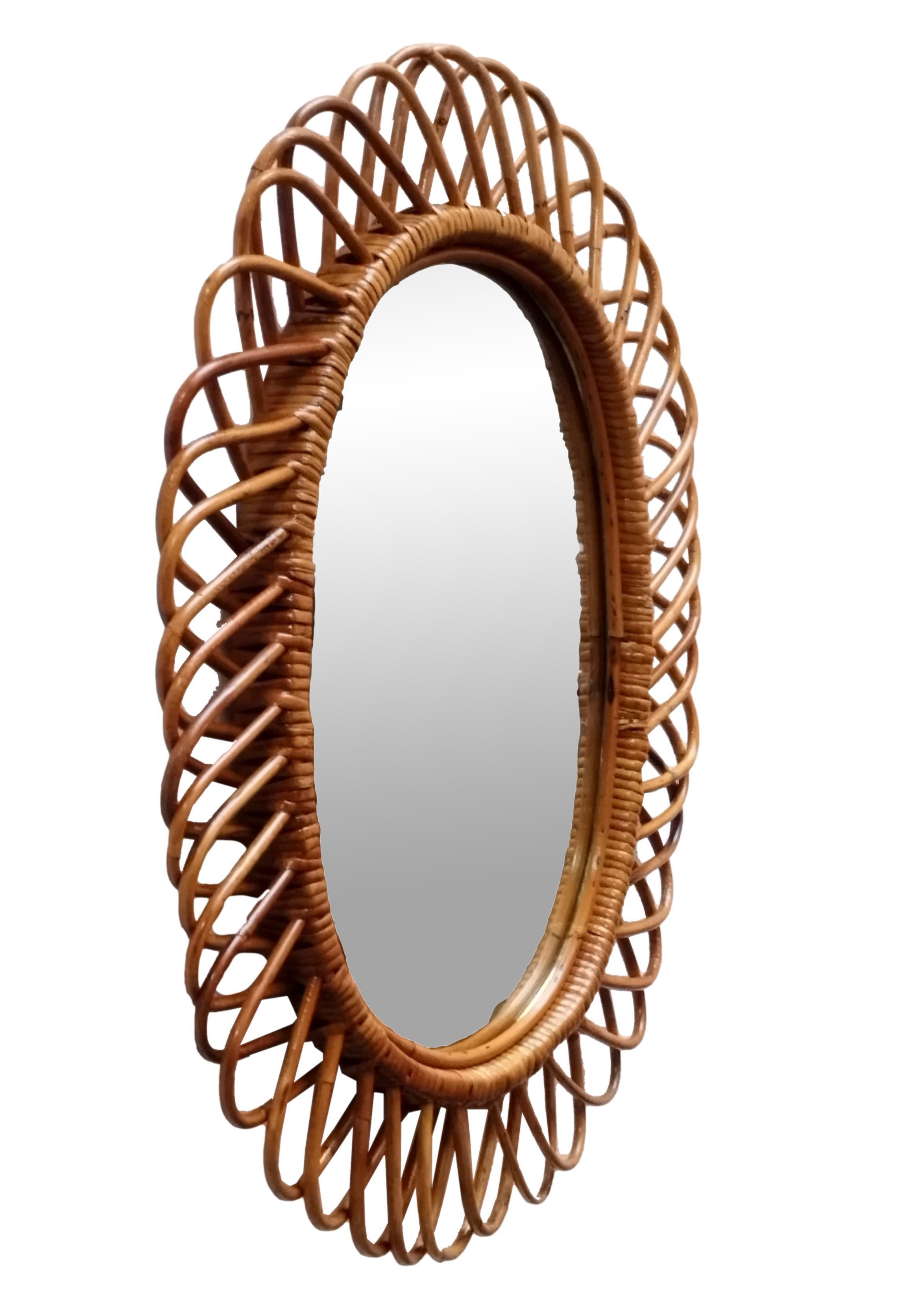 Italian rattan wall mirror (circa 1960s) by Franco Albini. The mirror has a complex weave of rattan in a series of horseshoe projections on the edge of the frame. There is a lovely aged patina on the rattan; the glass is intact.