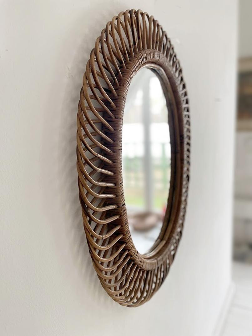 Italian rattan wall mirror (circa 1960s) by Franco Albini. The mirror has a complex weave of rattan in a series of horseshoe projections on the edge of the frame. There is a lovely aged patina on the rattan; the glass is intact.