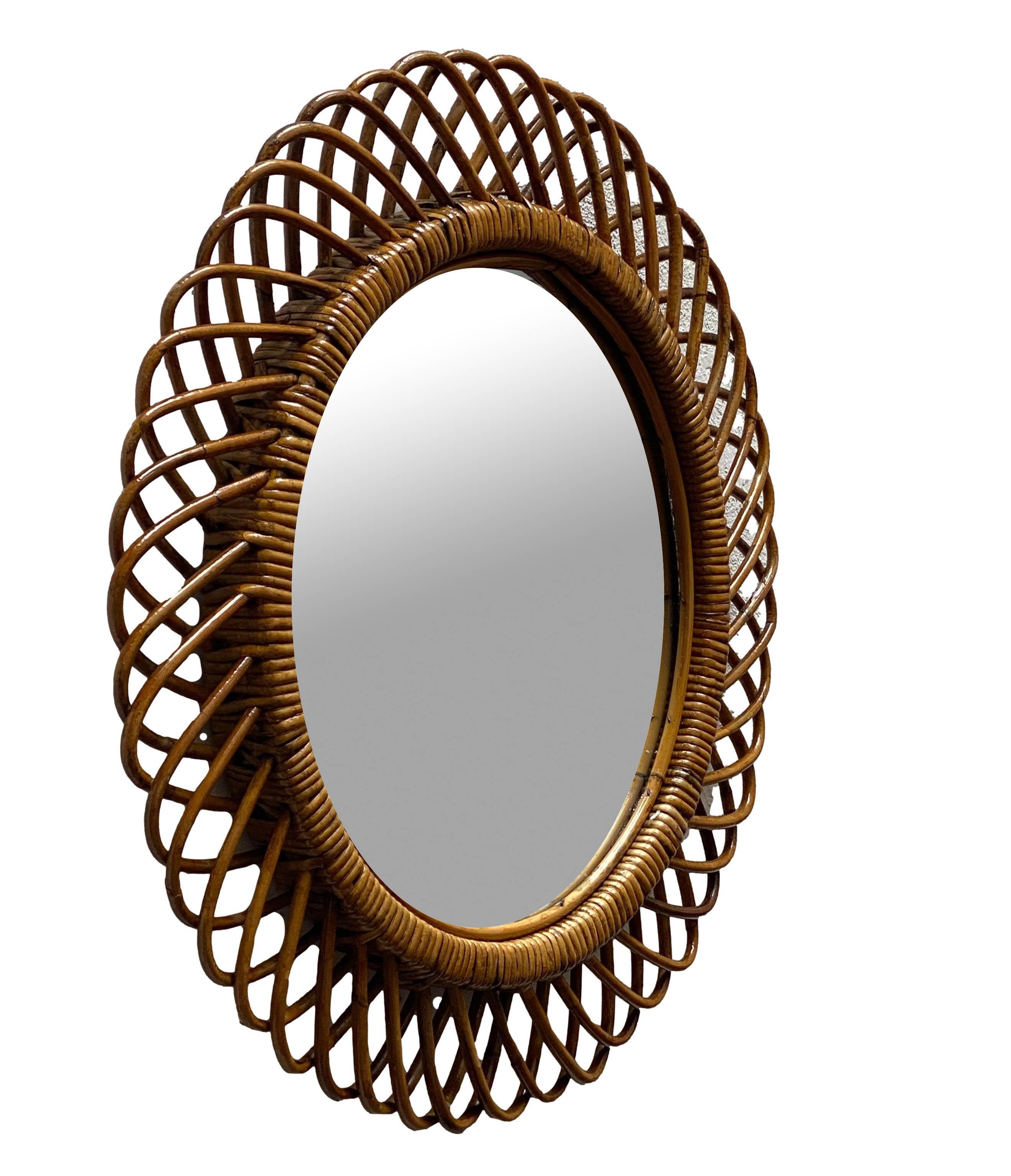Italian rattan wall mirror (circa 1960s) by Franco Albini. The mirror has a complex weave of rattan in a series of horseshoe projections on the edge of the frame. There is a lovely aged patina on the rattan.