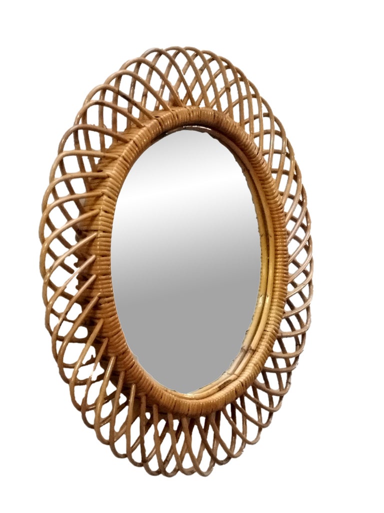 Italian rattan wall mirror  by Franco Albini. The mirror has a complex weave of rattan in a series of horseshoe projections on the edge of the frame. There is a lovely aged patina on the rattan. The glass is perfect