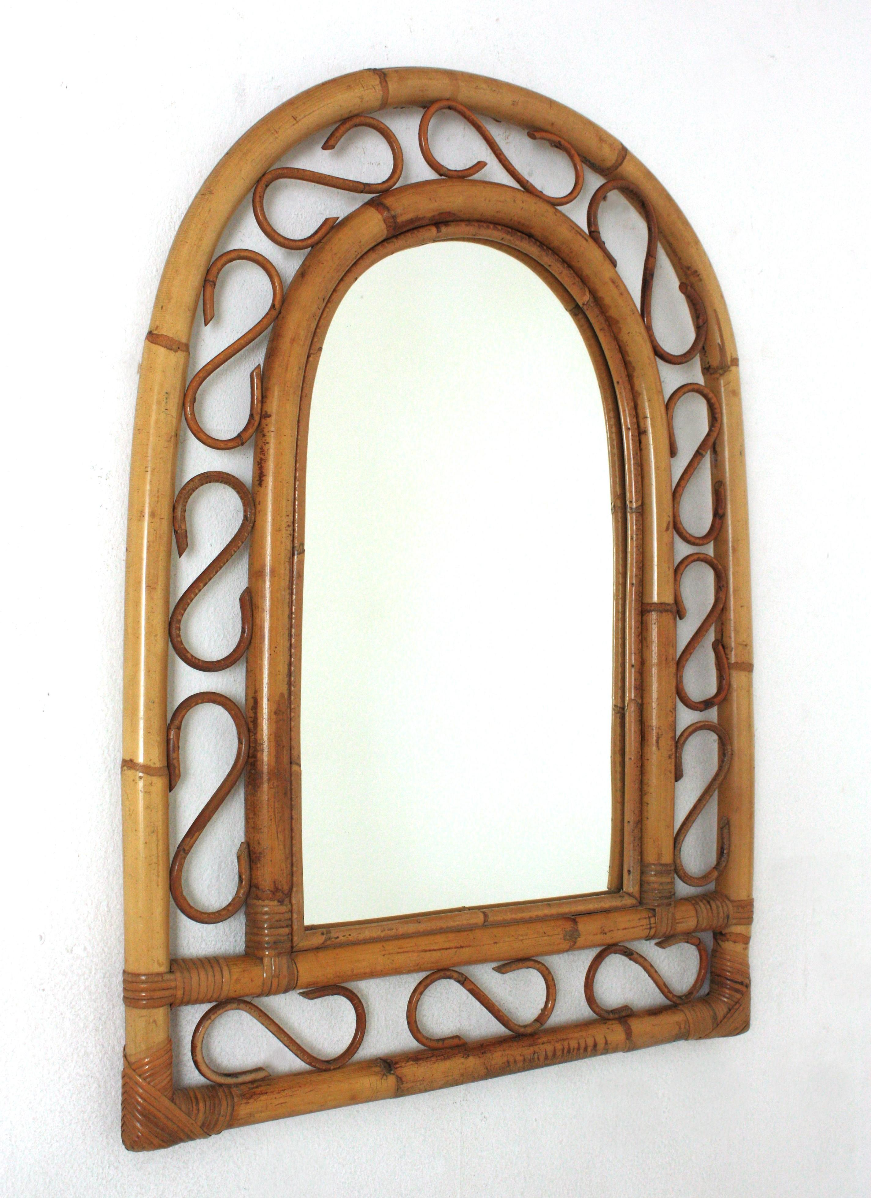 Miroir en bambou et en rotin fabriqué à la main dans le style Franco Albini de la modernité du milieu du siècle, avec un sommet arqué.
Ce miroir présente un double cadre en bambou avec des détails décoratifs en rotin entre les cannes de bambou.
Ce