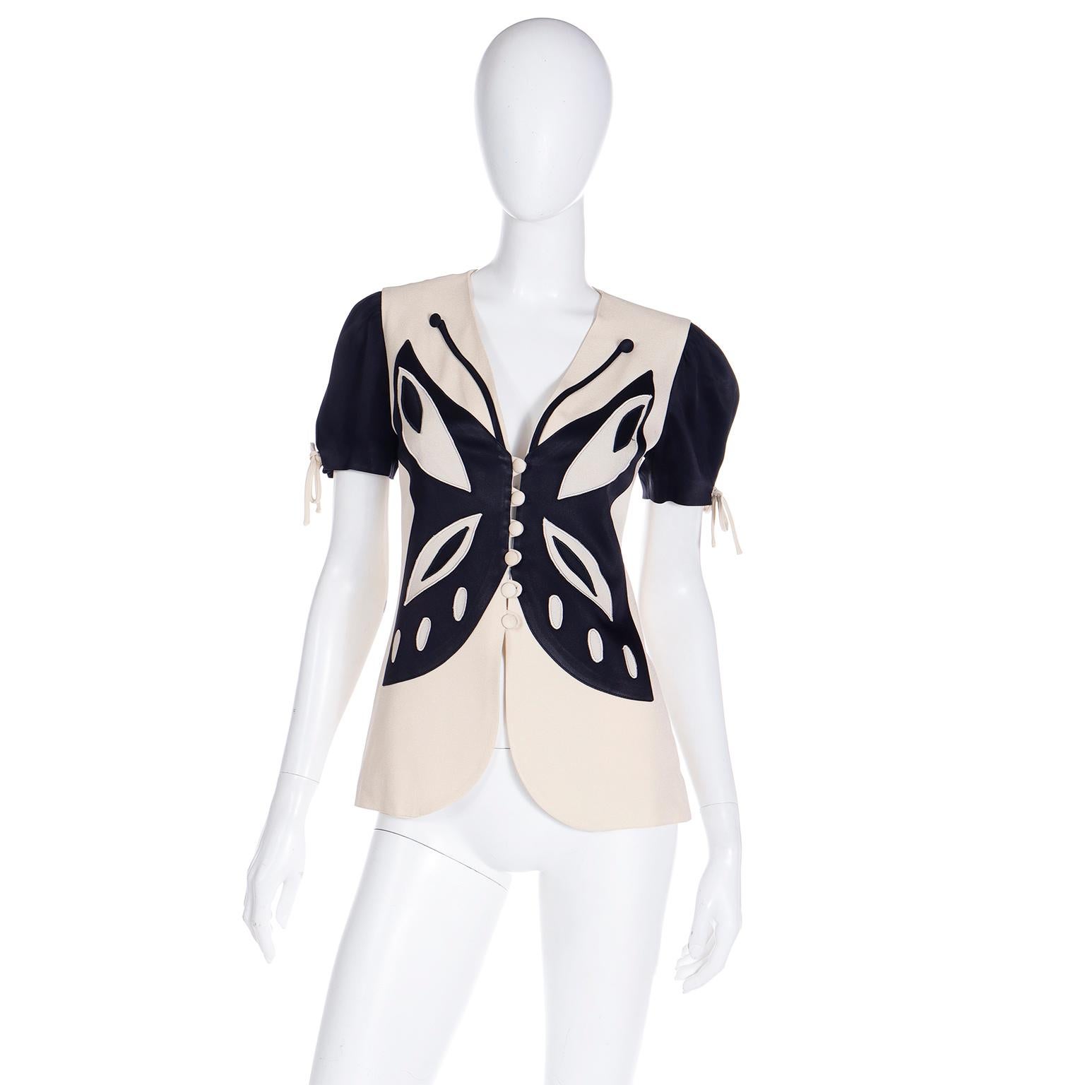 Franco Moschino used recurrent images and themes in his work and he loved butterflies. This black and cream top or short sleeve jacket has black sleeves and a black applique of a large butterfly on the front. This is a great example of Moschino's