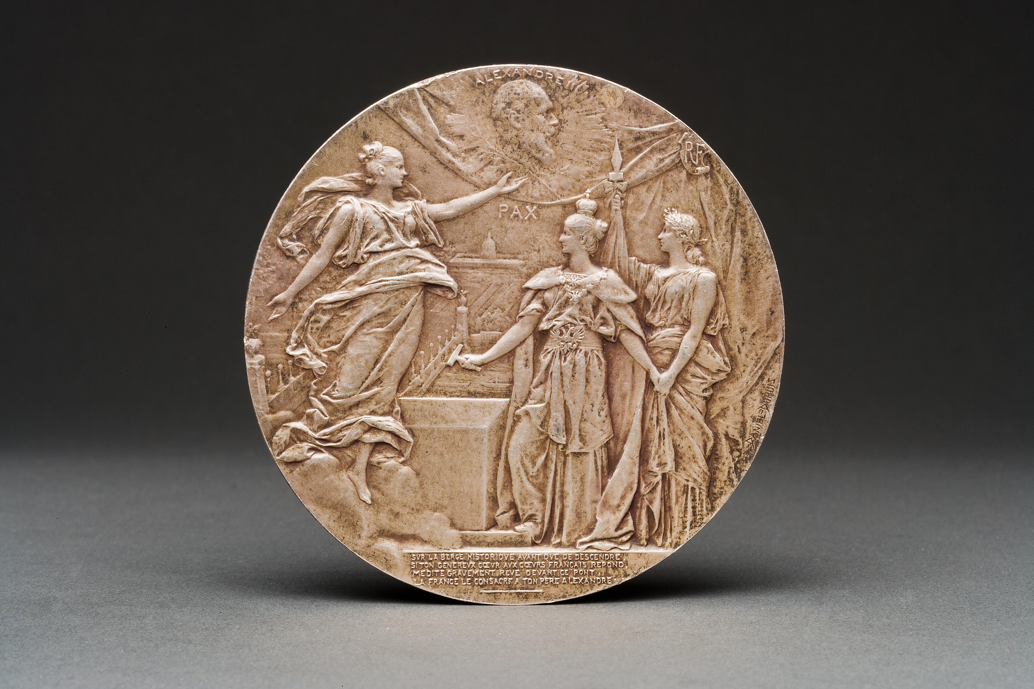 En bronze argenté, un médaillon de table commémorant la visite de Nicolas et Alexandra à Paris pour poser la première pierre du pont Alexandre III en 1896, avec des inscriptions dédicatoires en français, au recto et au verso.

Français, daté du 7