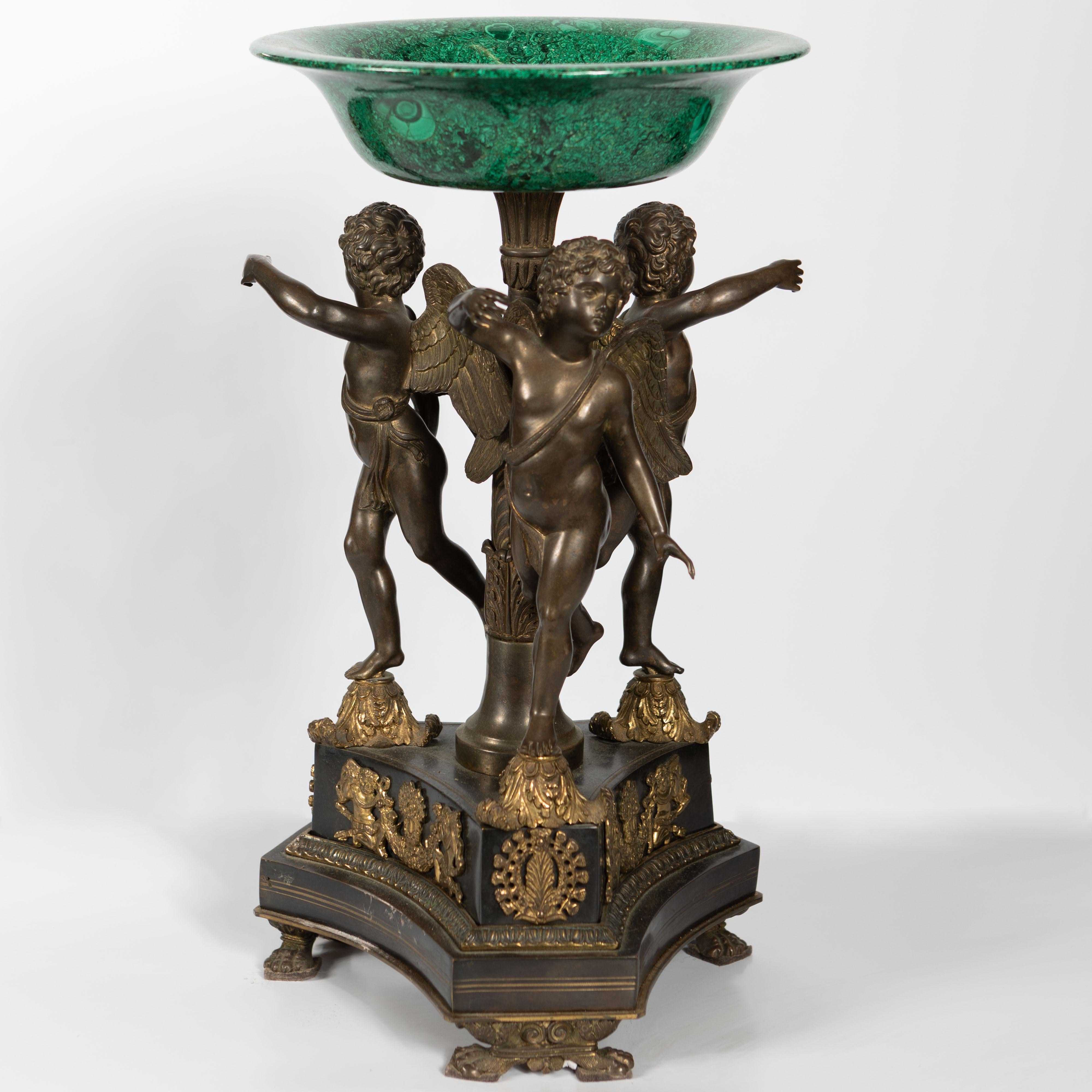 Cet extraordinaire centre de table franco-russe en malachite et en bronze du XIXe siècle présente trois putti ailés délicatement sculptés, chacun tenant un sommet en malachite, créant ainsi une œuvre d'art véritablement captivante et opulente. Le